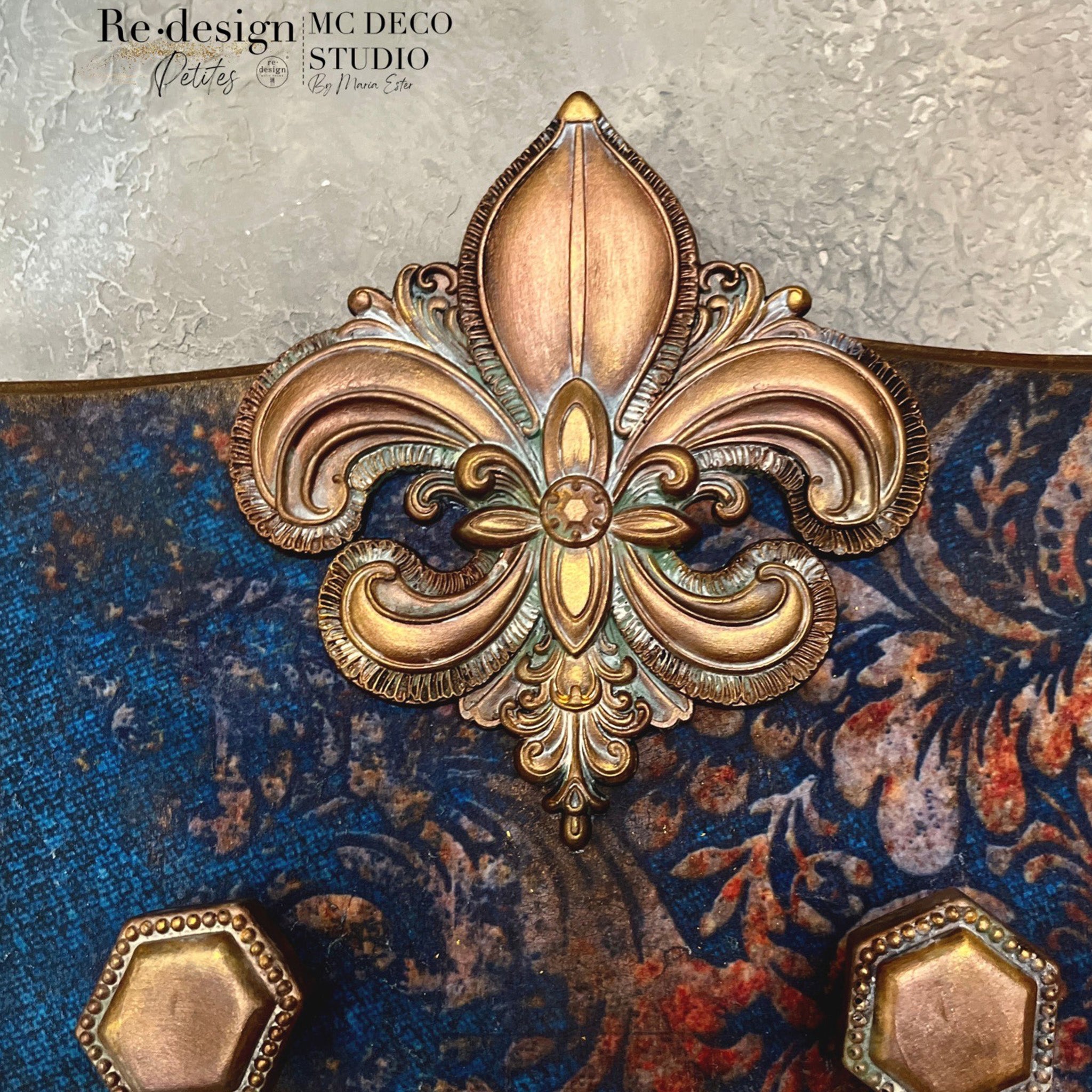 A close-up of a craft created by MC Deco Studio features ReDesign with Prima's Salon De La fleur de lis painted bronze on it.