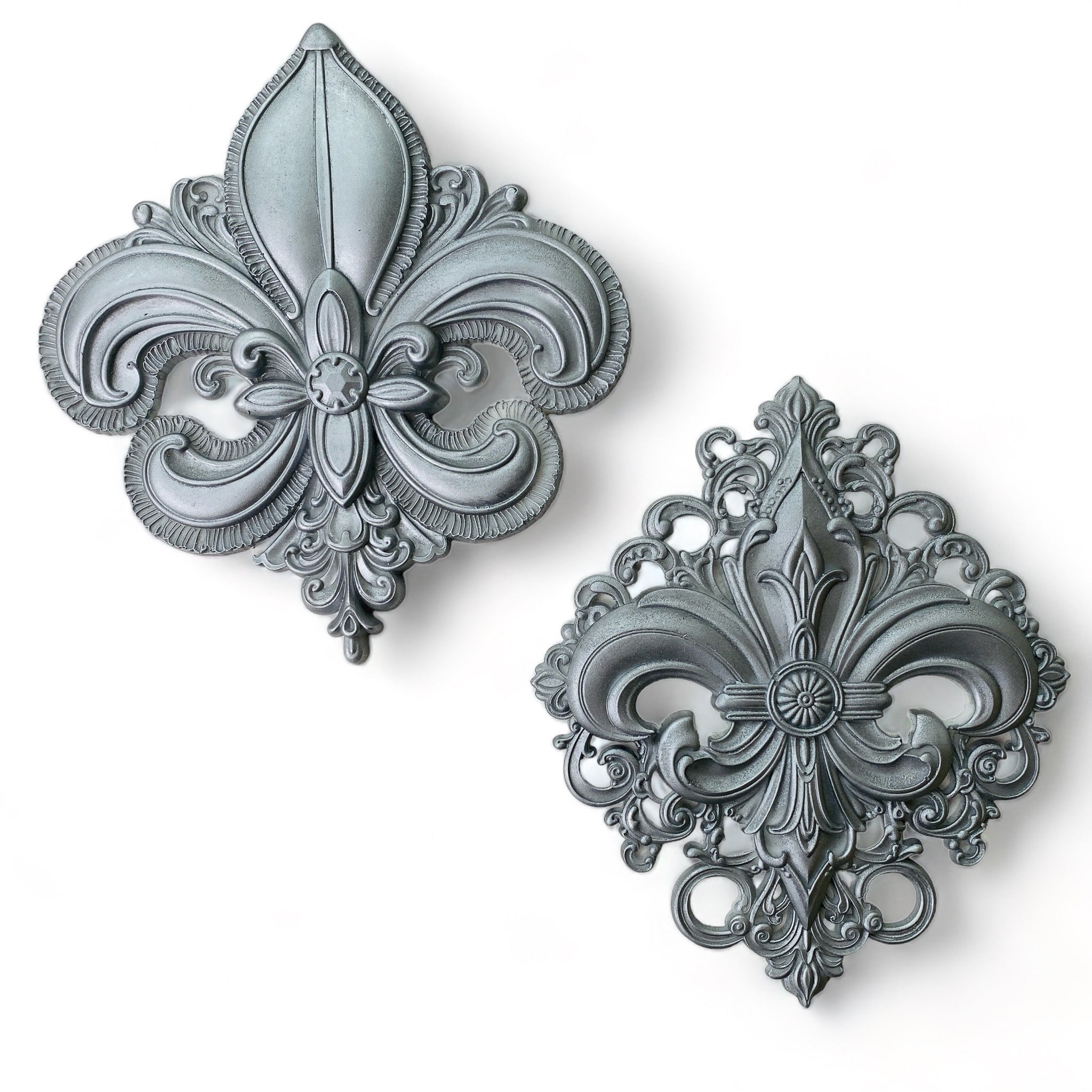 Silver-colored silicone mold castings of 2 large ornate Fleur de Lis designs are against a white background.