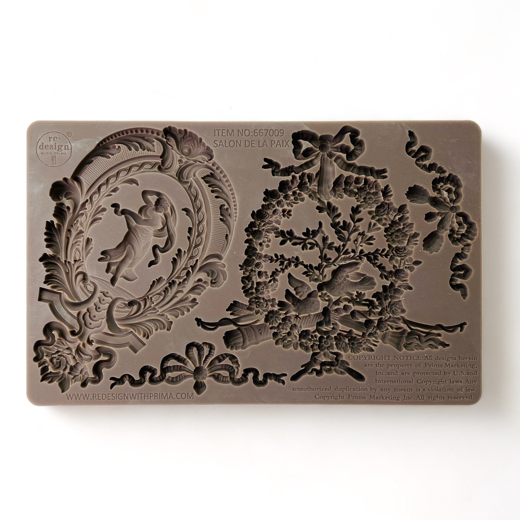 A brown silicone mold that features 2 bows, an ornate oval medallion and an ornate wreath is against a white background.