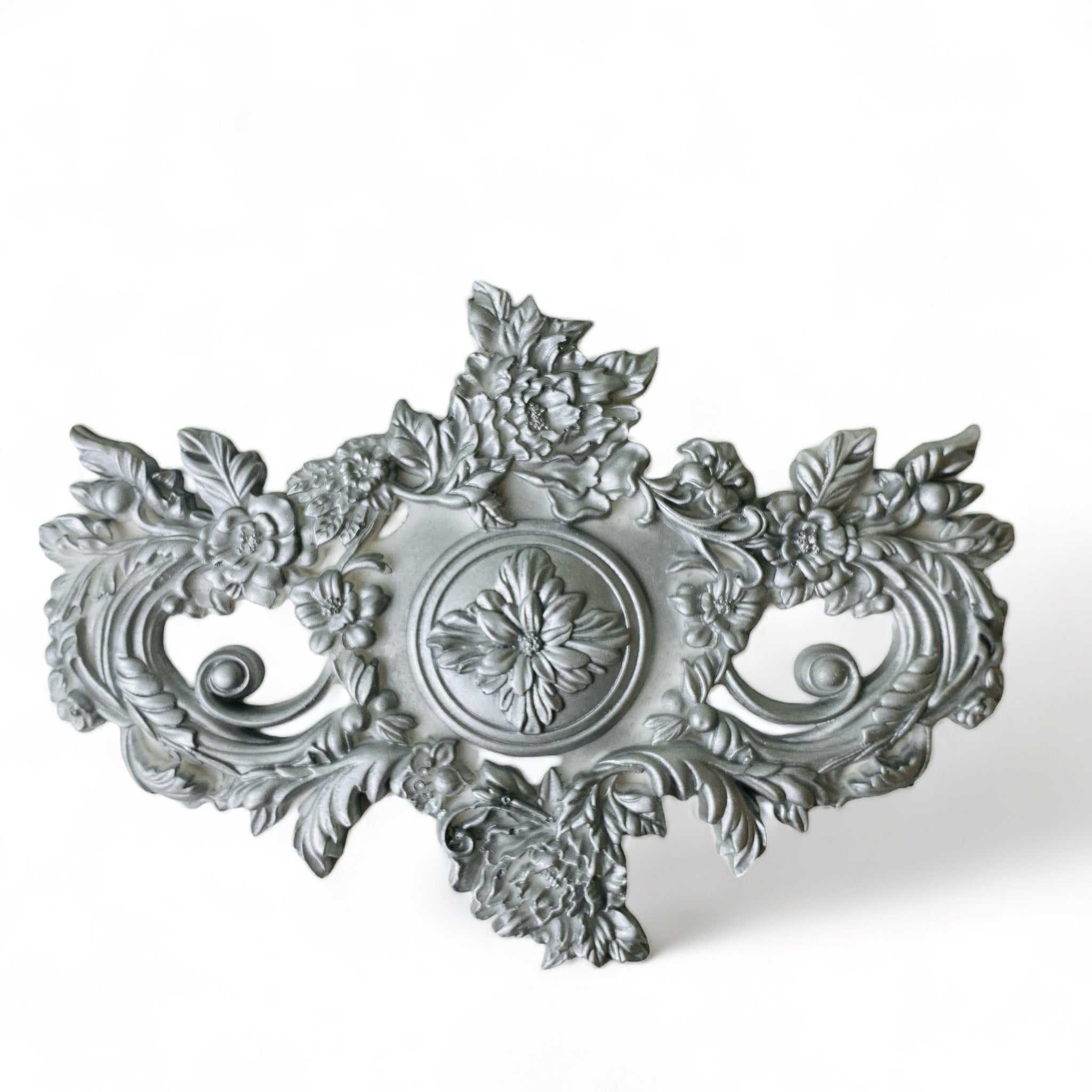 A silver-colored silicone mold casting of a large ornate floral accented medallion center piece is against a white background.