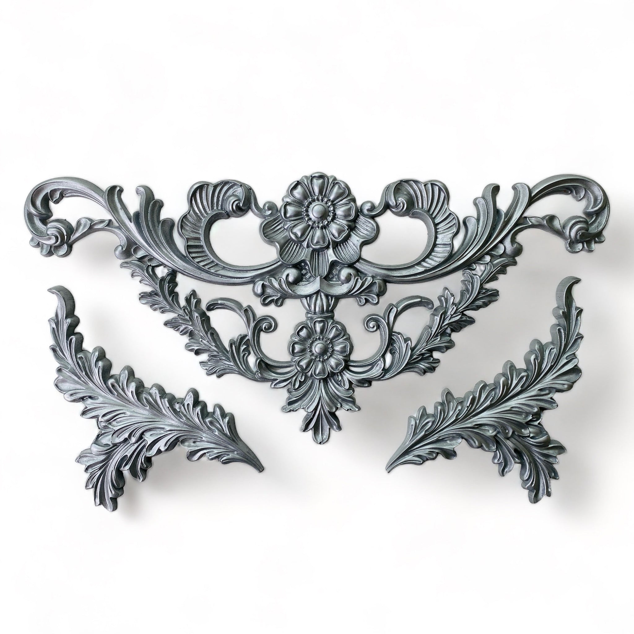 Silver-colored silicone mold castings of a large ornate scroll floral leaf accent piece and 2 leaf plumes are against a white background.