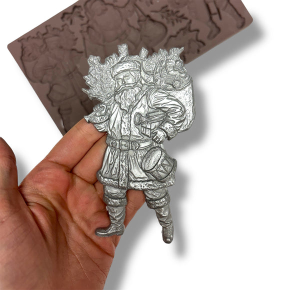 Silver santa held by a hand against a white background with a blurry silicone mold