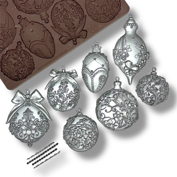 Decorative silver ornaments with intricate designs next to a mold on a white background