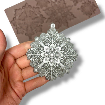 Decorative silver pendant held by a hand with a mold in the background