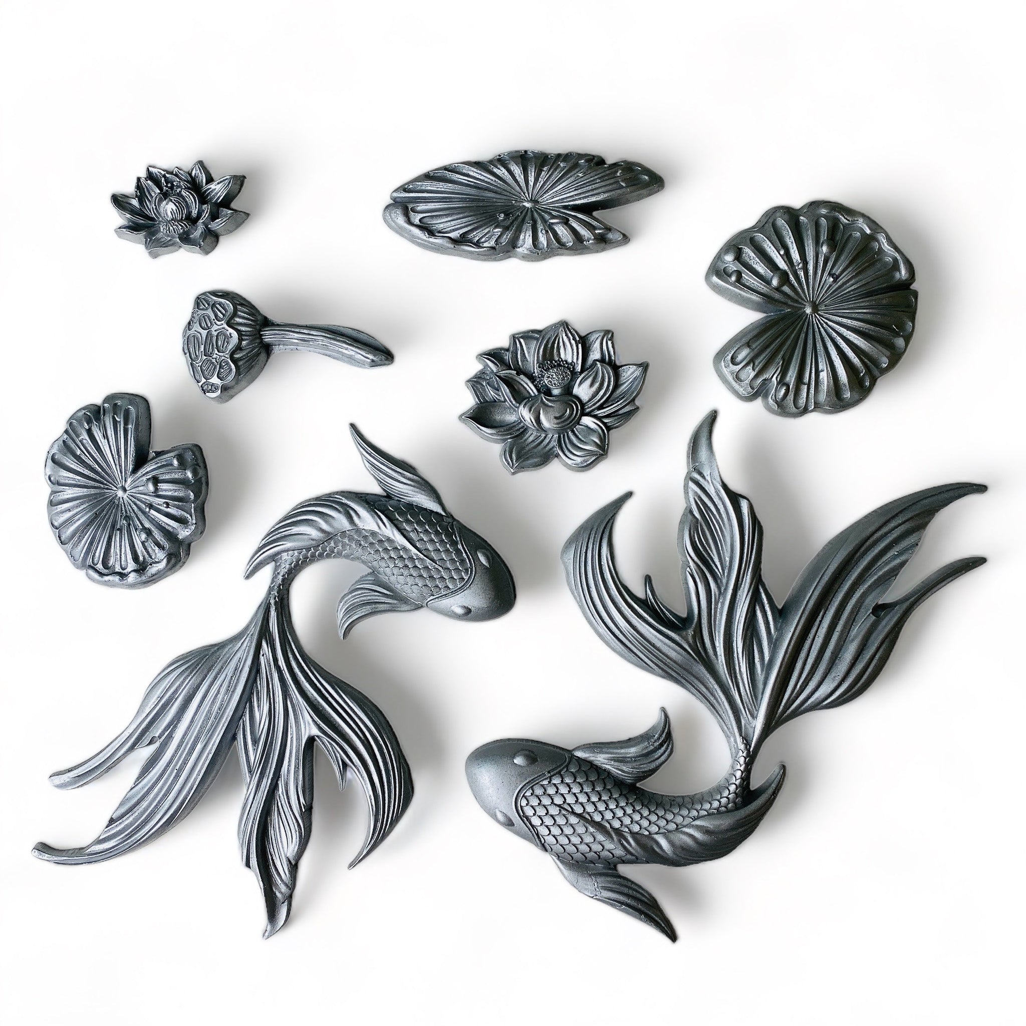 Silver-colored silicone mold castings featuring 2 intricately-detailed koi fish, surrounded by water lilies and lily pads are against a white background.