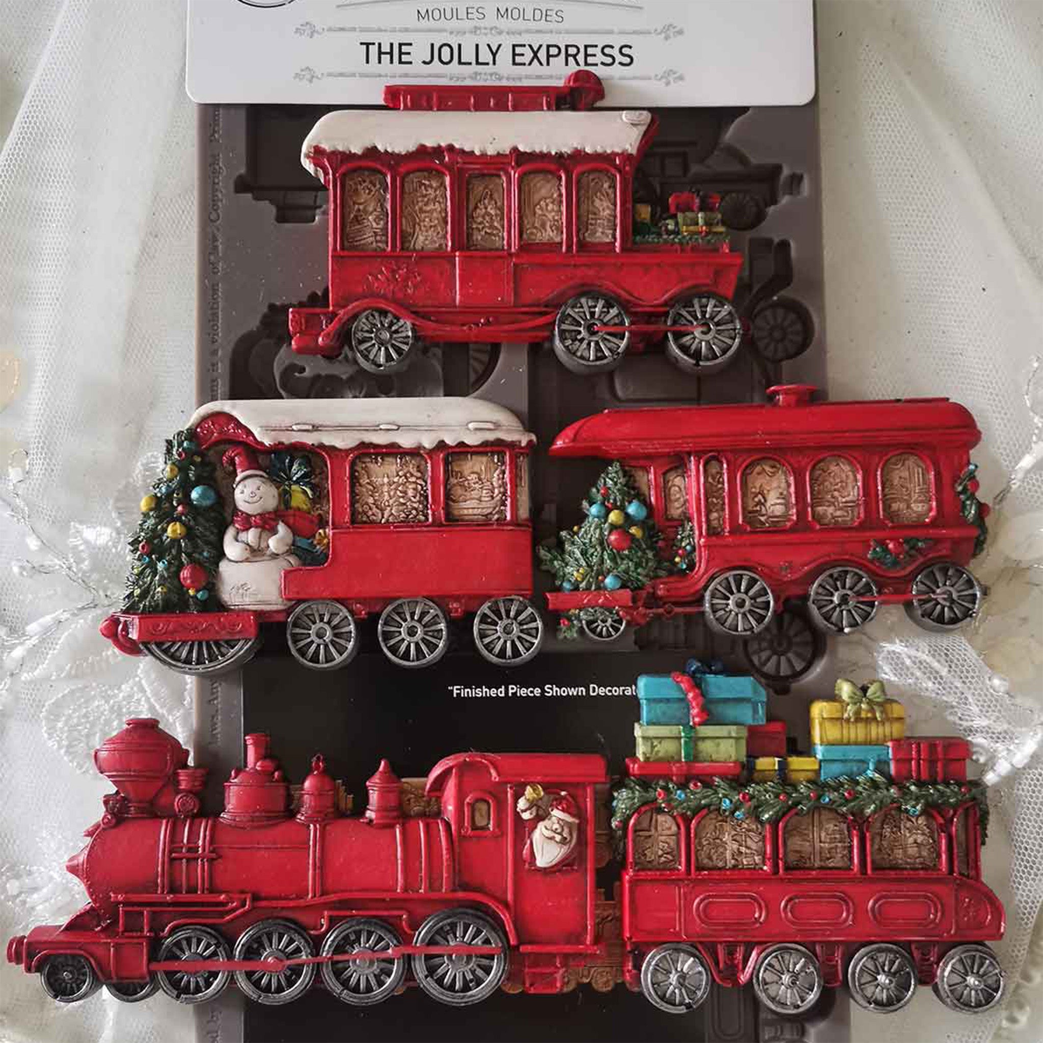 A package of ReDesign with Prima's The Jolly Express silicone mold and colorful castings created by Casamia are against a white lace background.