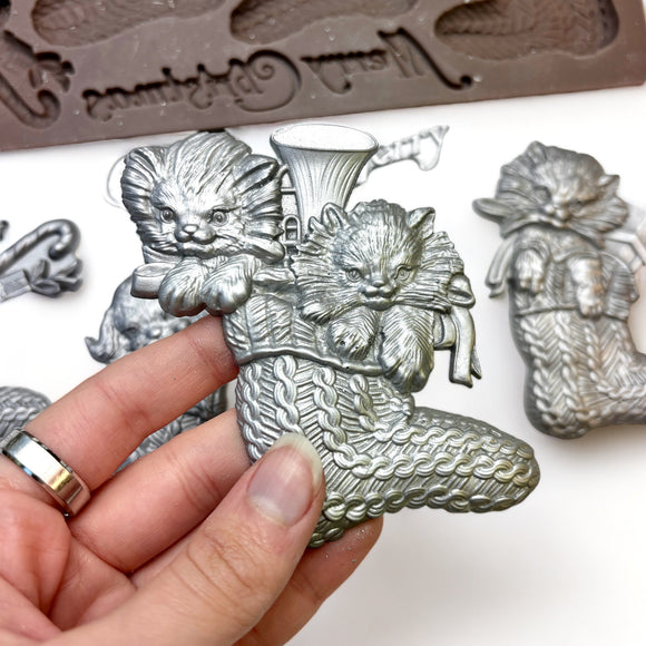 A close-up of a hand holding a silver colored casting made from ReDesign with Prima's Twinkle Paws silicone mold is against a white background.