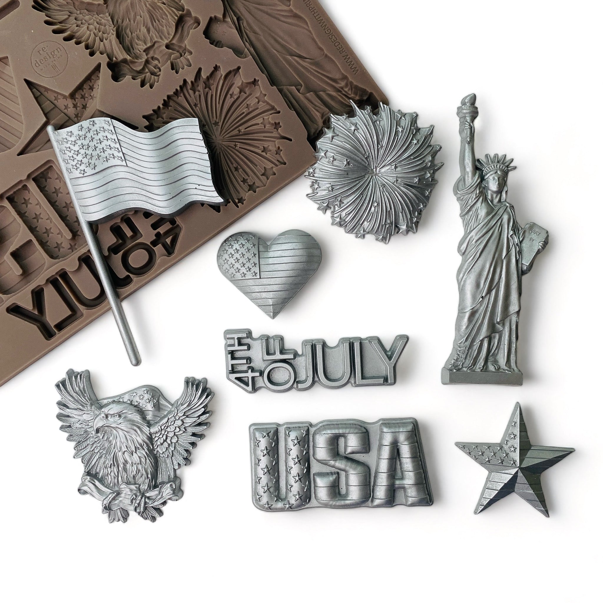 A brown silicone mold and silver colored castings of ReDesign with Prima's Happy 4th silicone mold are against a white background. 