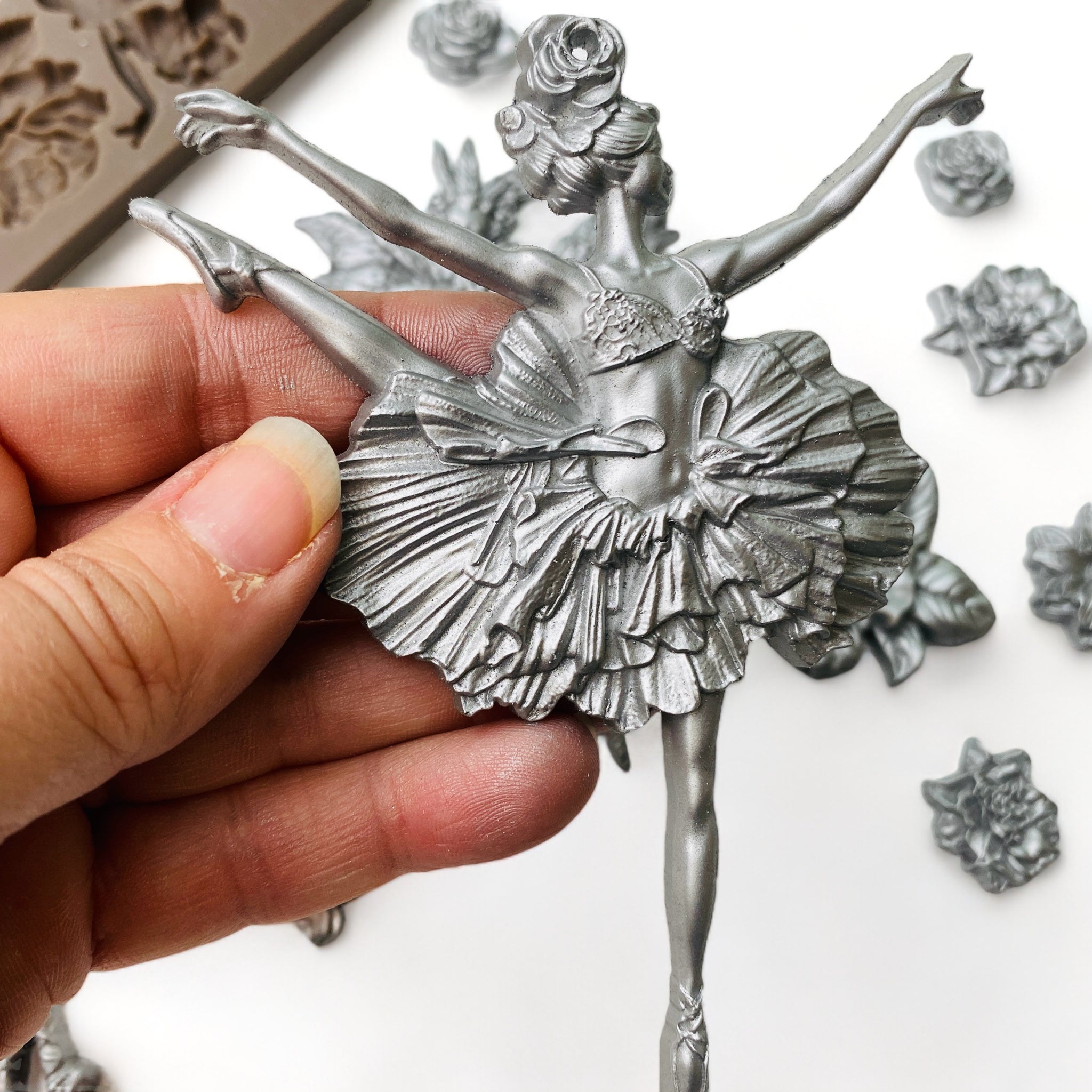 A hand is shown holding a silver colored casting of a ballerina from ReDesign with Prima's Angelic Twirl silicone mold.