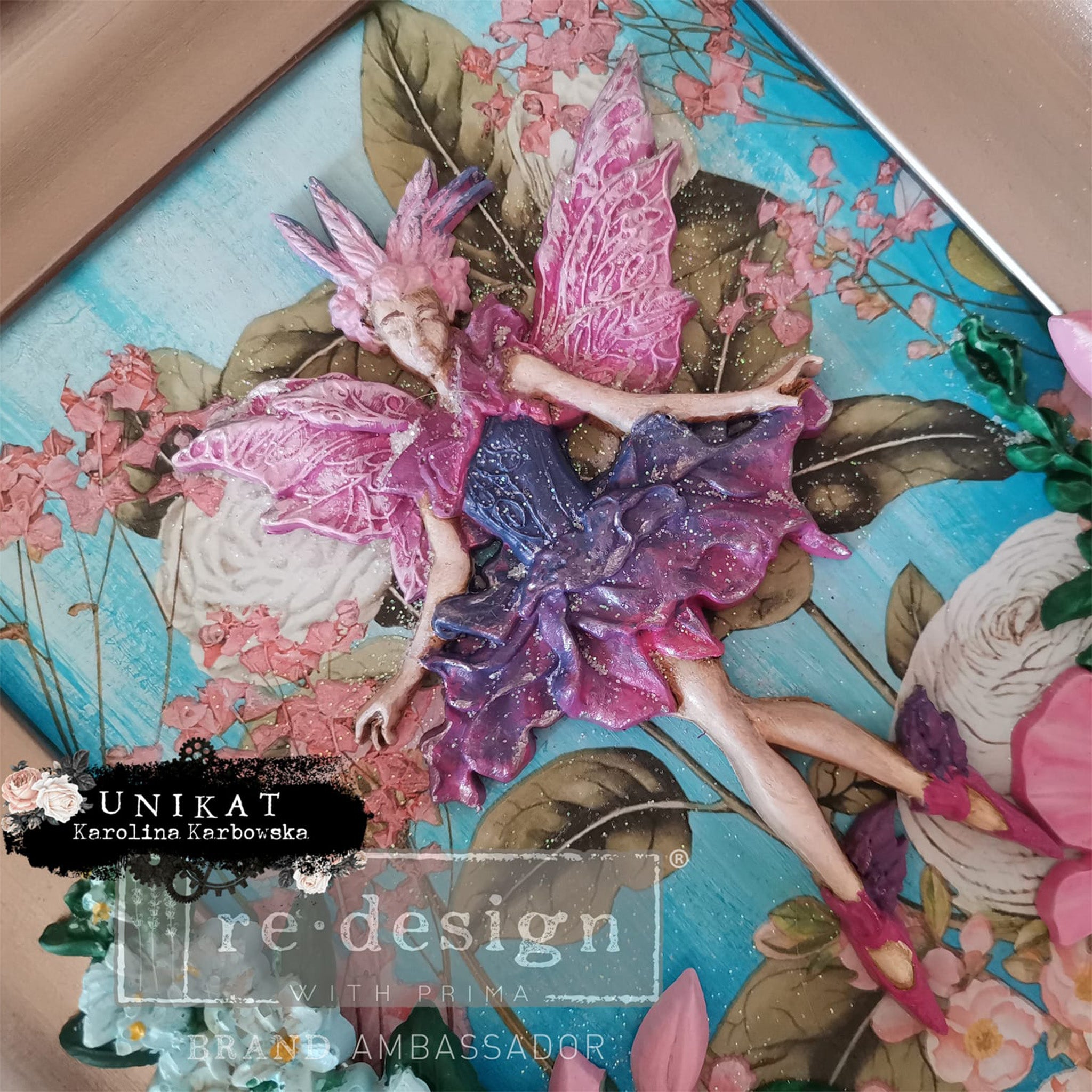 A colorful casting created by Unikat Karolina Karbowska using ReDesign with Prima's Angelic Twirl silicone mold is shown against a colorful floral background in a picture frame.