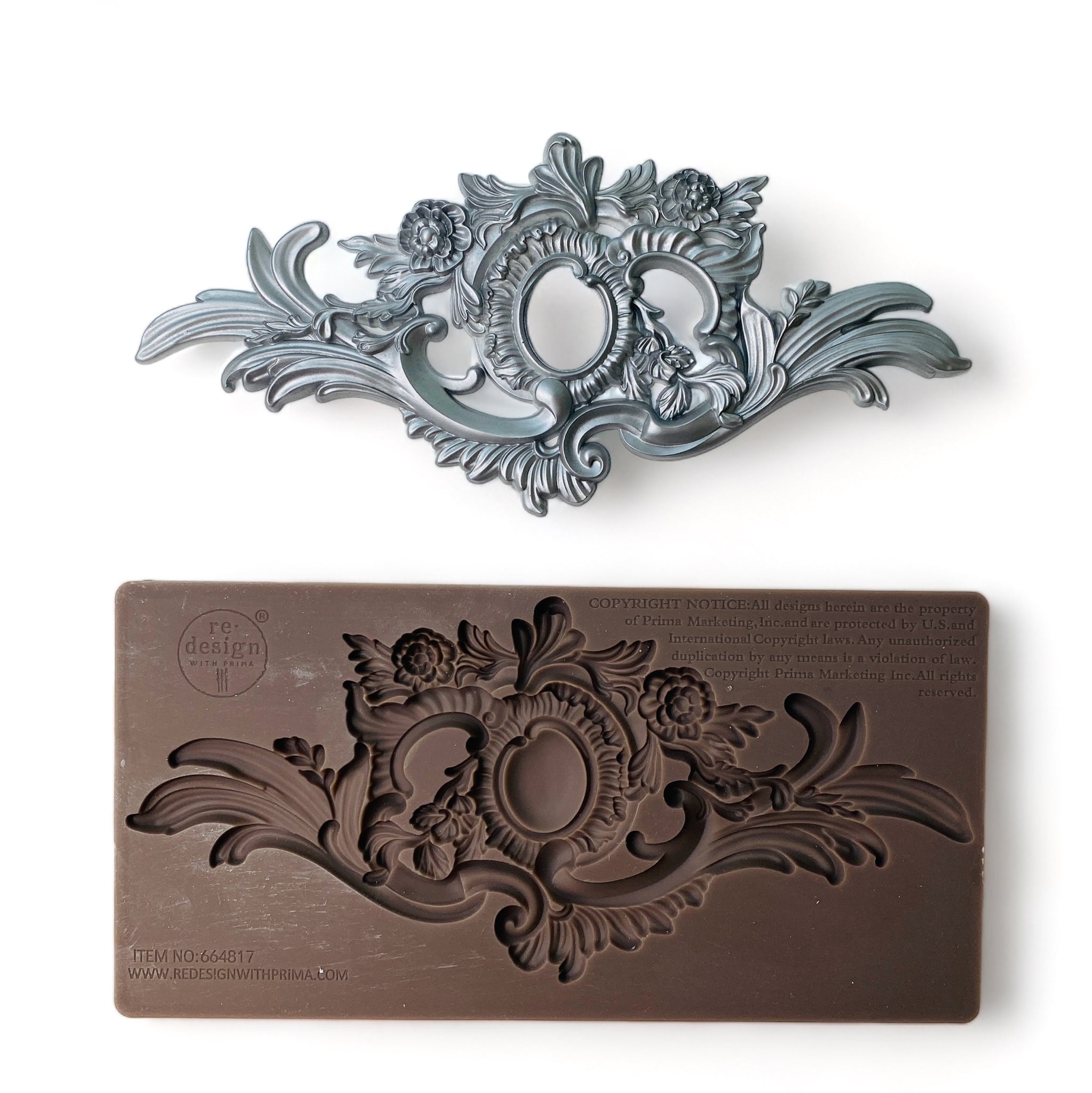 A brown silicone mold and silver colored casting that  features a unique ornate flourish and central medallion are against a white background.