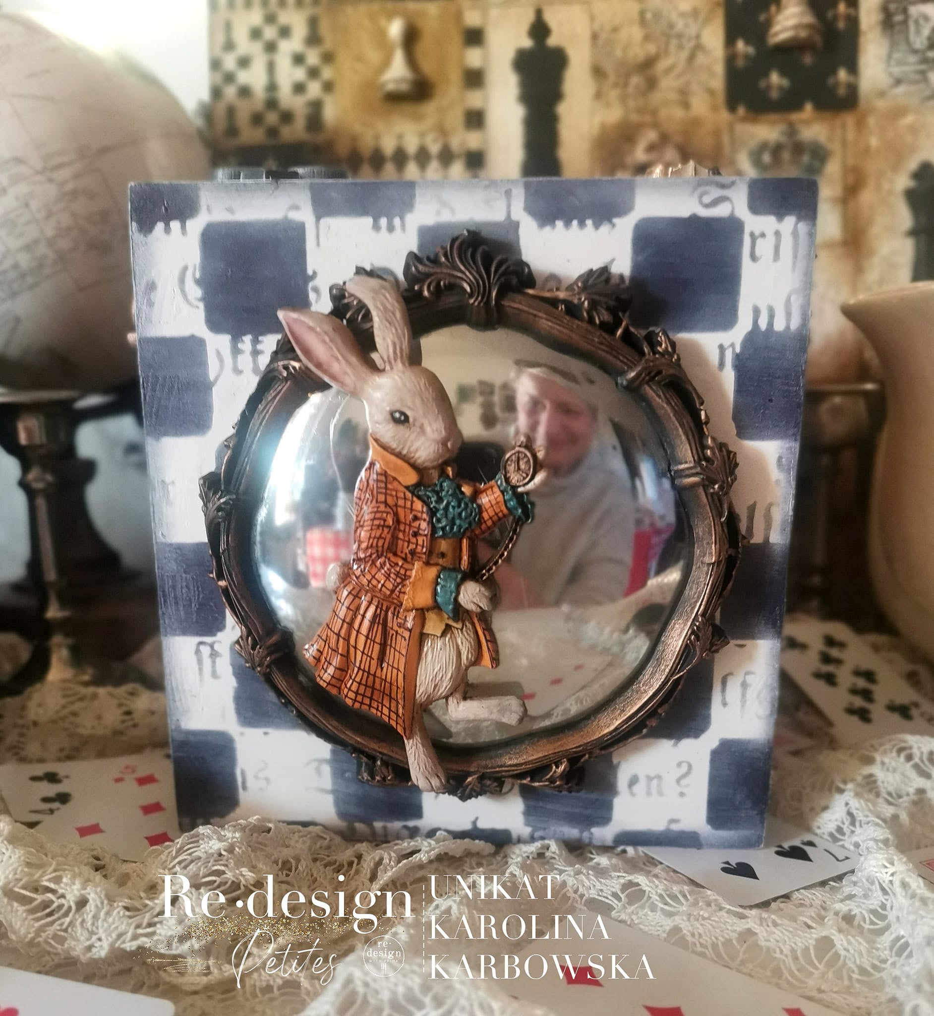 A small fish-eye mirror on a checkered piece of wood created by Unikat Karolina Karbowska features ReDesign with Prima's Astrid silicone mold around the mirror and a silicone mold casting of rabbit in a waistcoat on it.