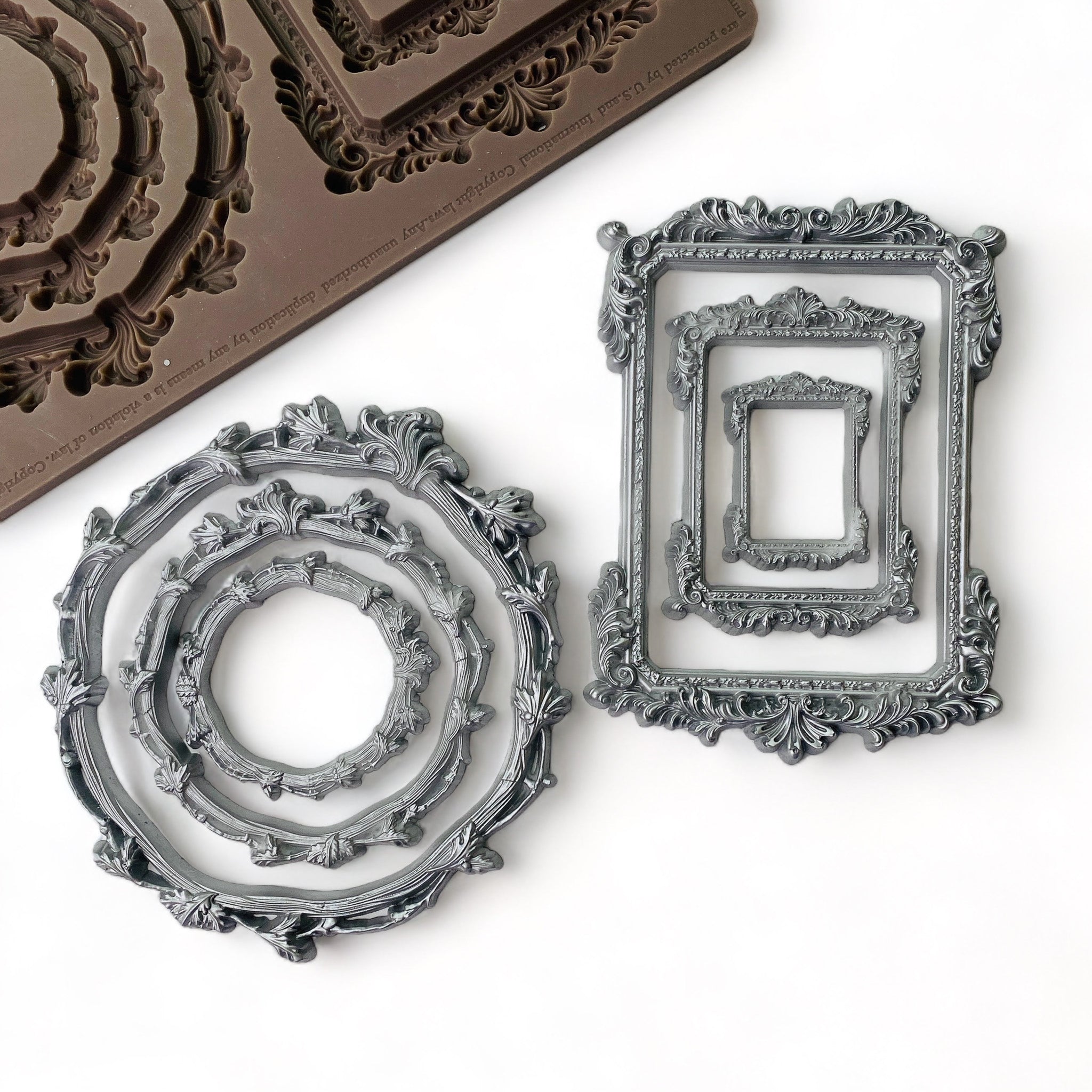 A brown silicone mold and silver colored castings of 6 ornate frames, 3 round and 3 rectangular, are against a white background.