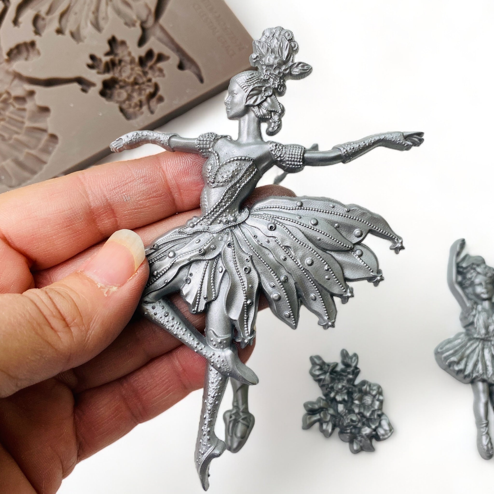 A hand is shown holding a silver colored casting of a ballerina from ReDesign with Prima's Celestial Grace silicone mold.