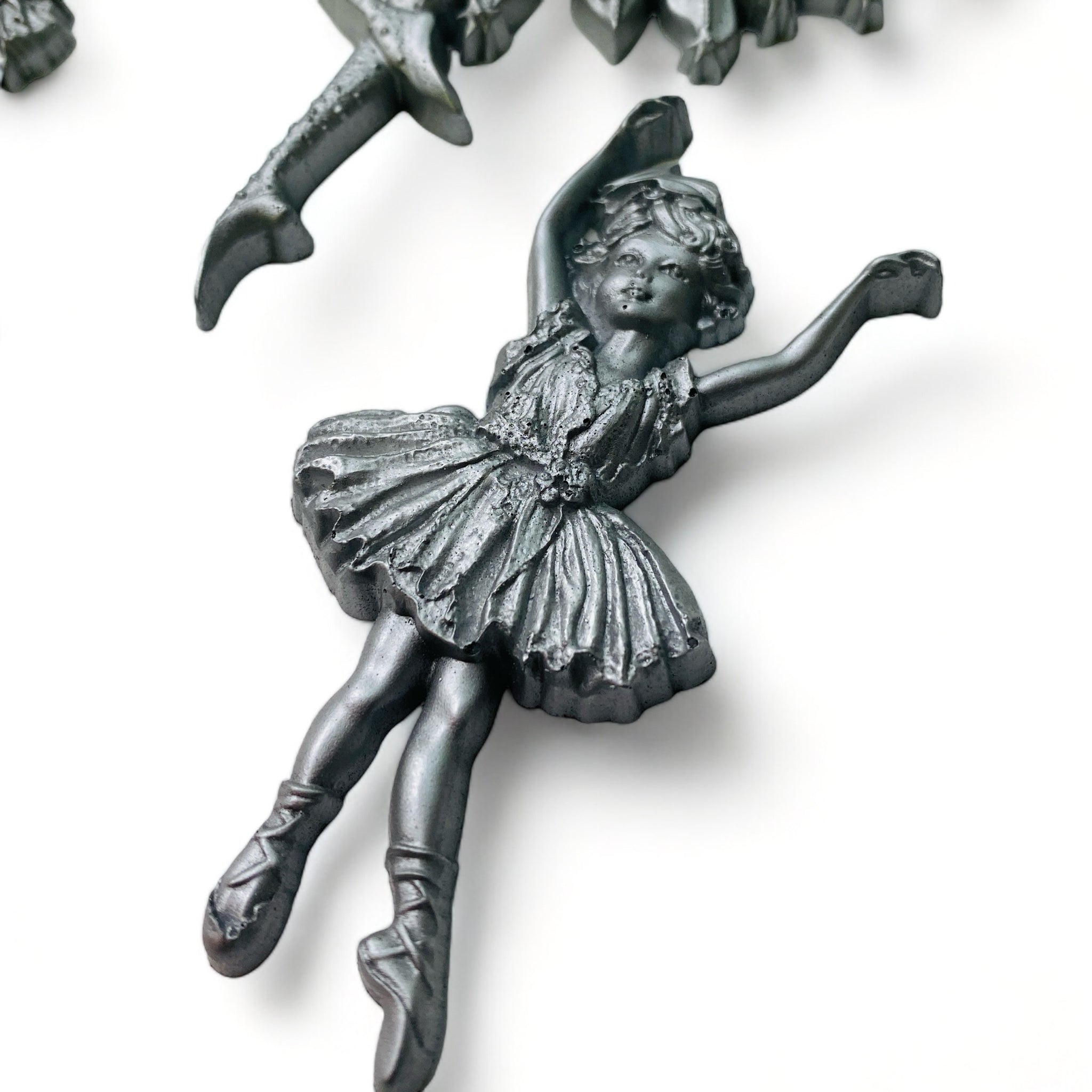 A close-up of a silver colored silicone mold casting of a child ballerina is against a white background.