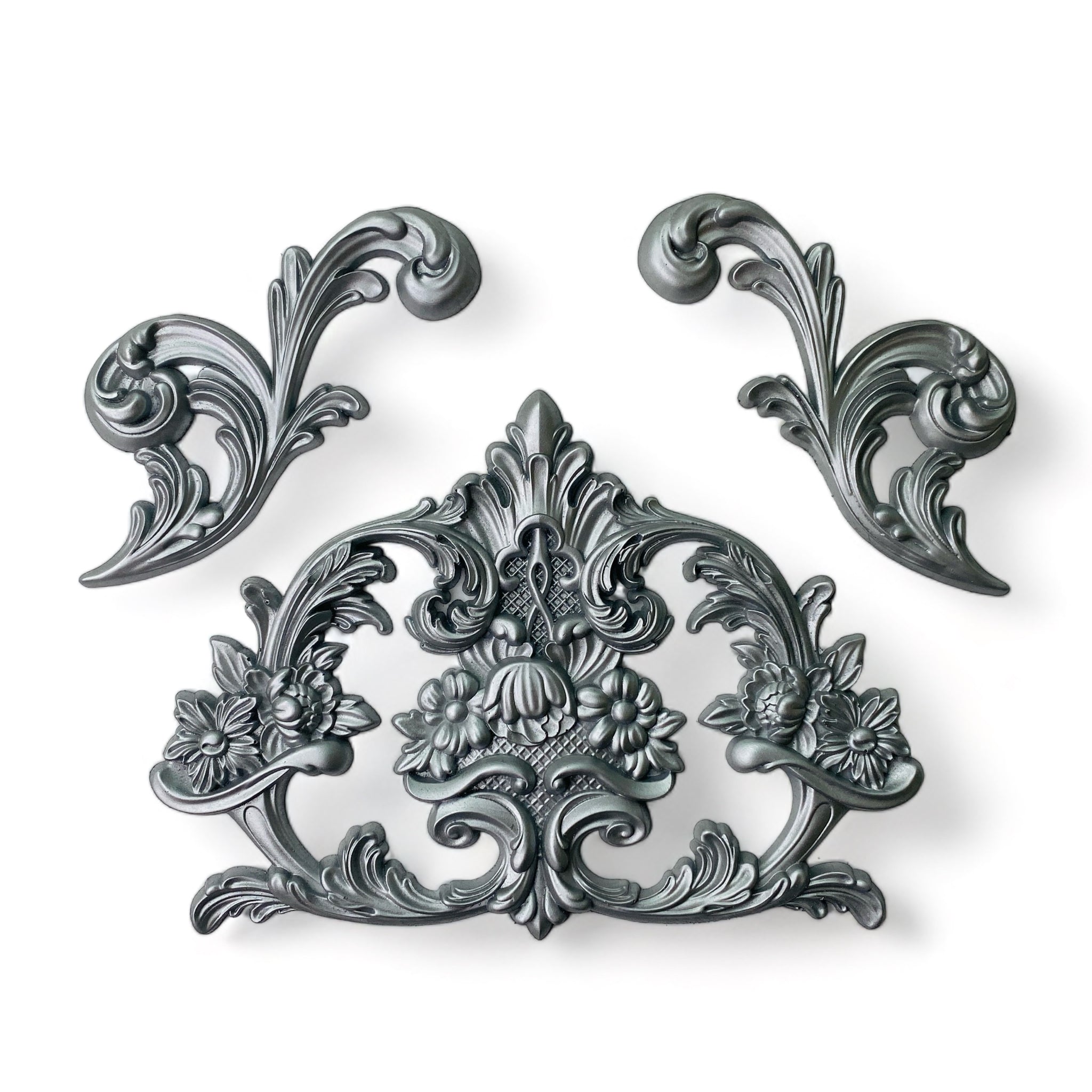Silver colored castings of 2 swirl scrolls and a flourish crest are against a white background.