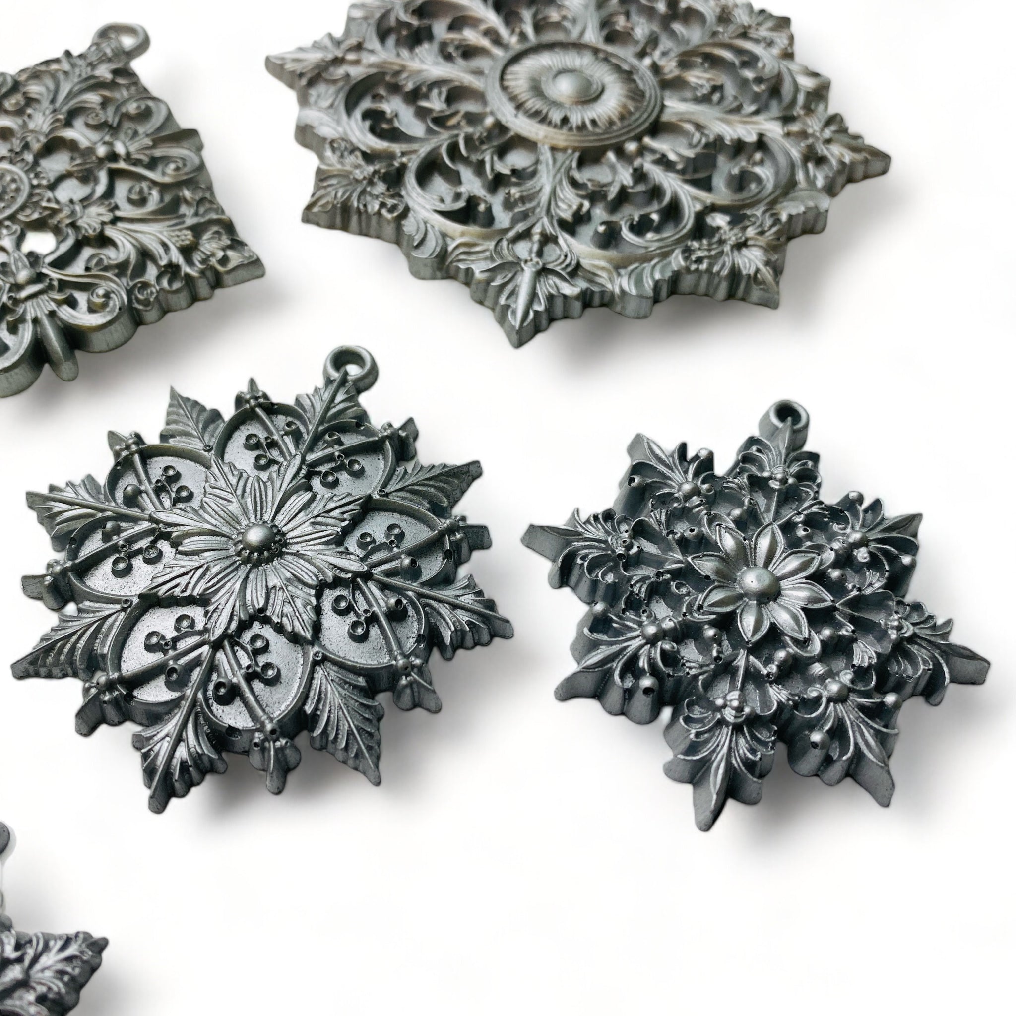 A close-up of silver colored castings from ReDesign with Prima's Dazzling Ornates silicone mold are against a white background.