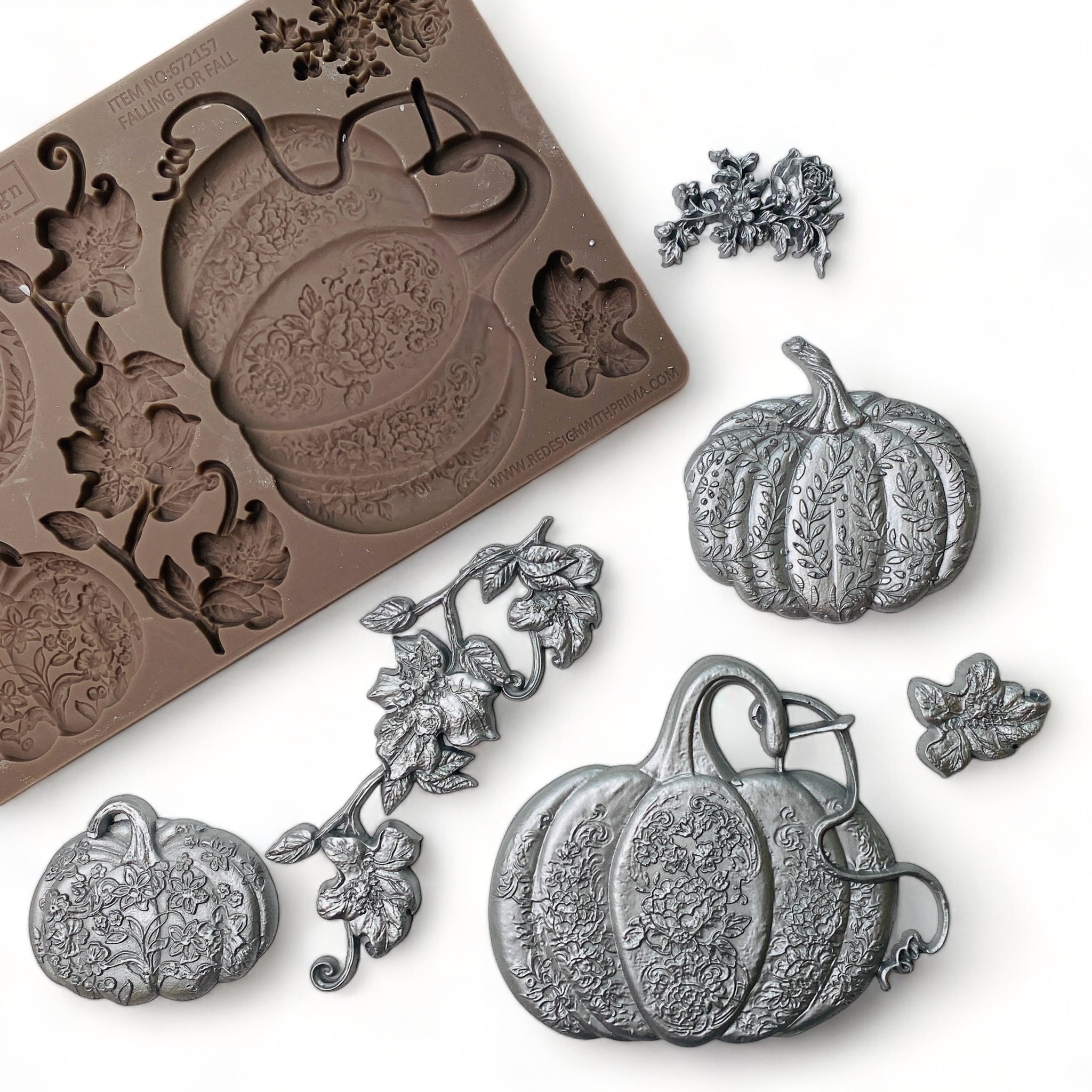 A brown silicone mold and silver colored castings of 3 pumpkins and some loose vines and leaves are against a white background.