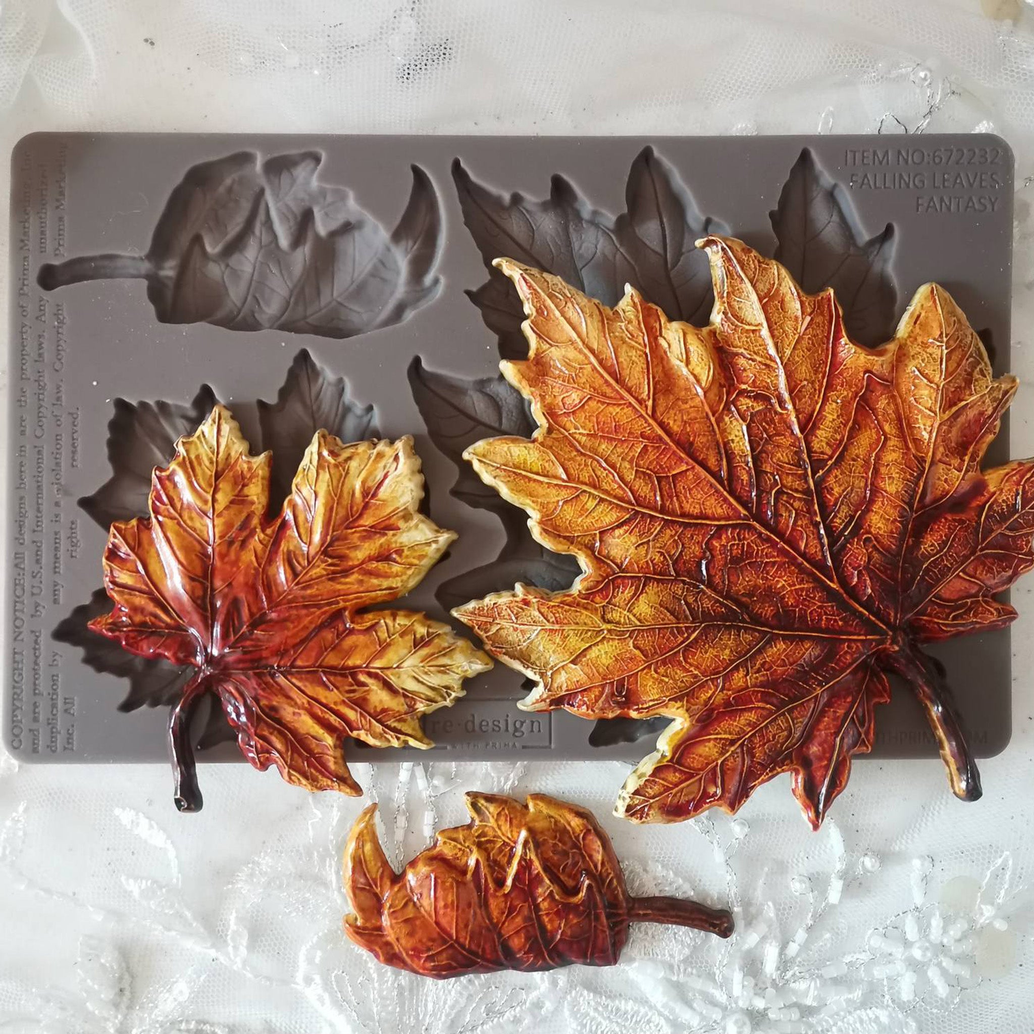 A brown silicone mold and fall colored castings of 3 maple leaves are against a white background.