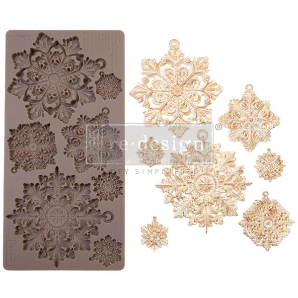 A brown silicone mould and gold/white castings of 7 ornately detailed snowflakes are against a white background.