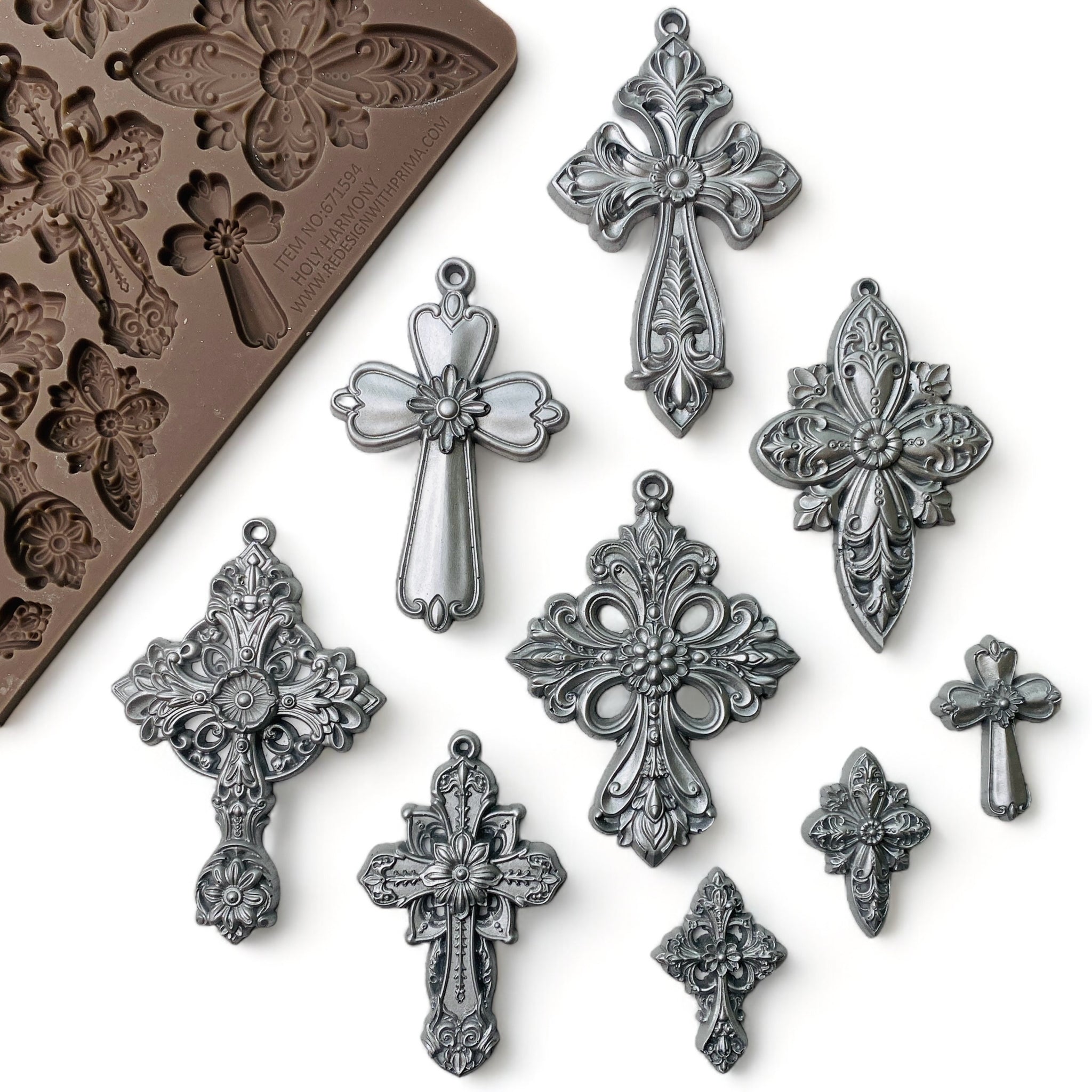 A brown silicone mold and silver colored castings of 9 varying sizes of ornate vintage crosses are against a white background.