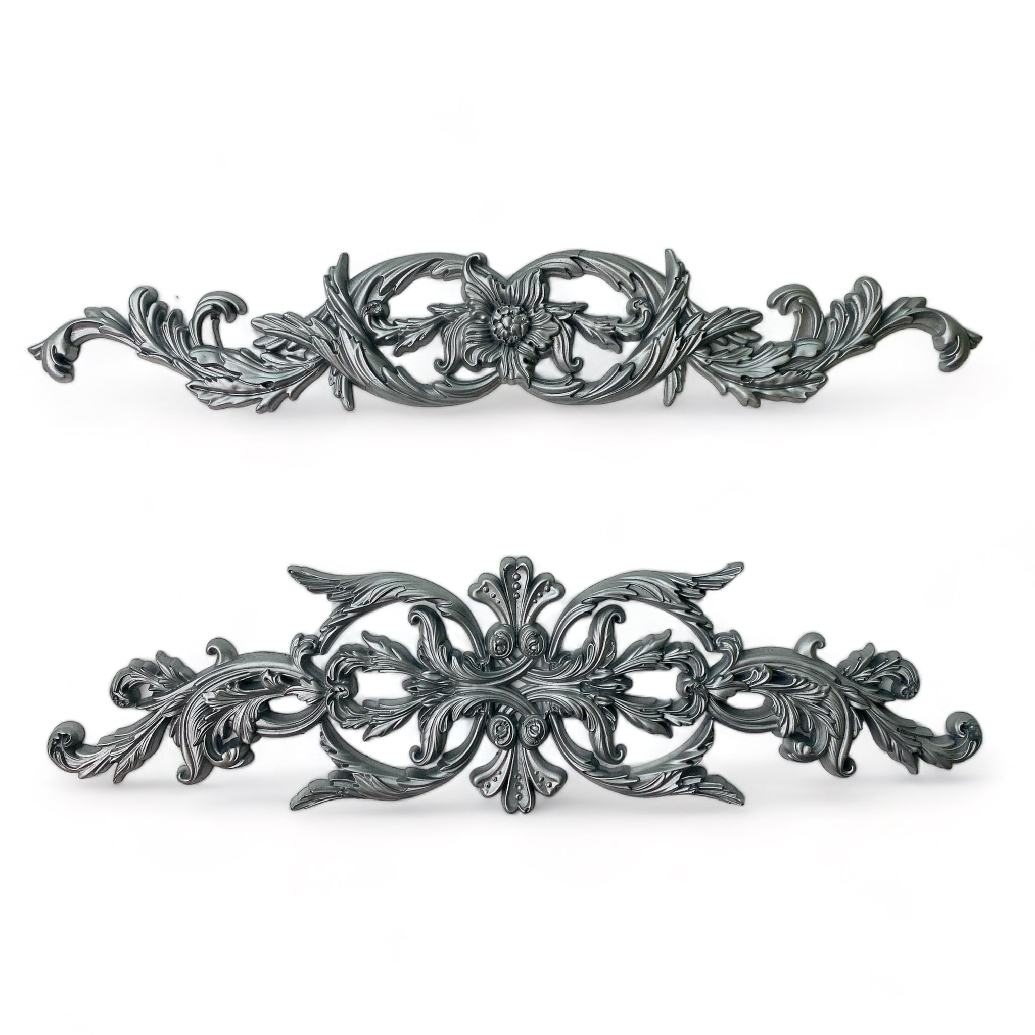 Silver colored castings of 2 ornate scrolls are against a white background.