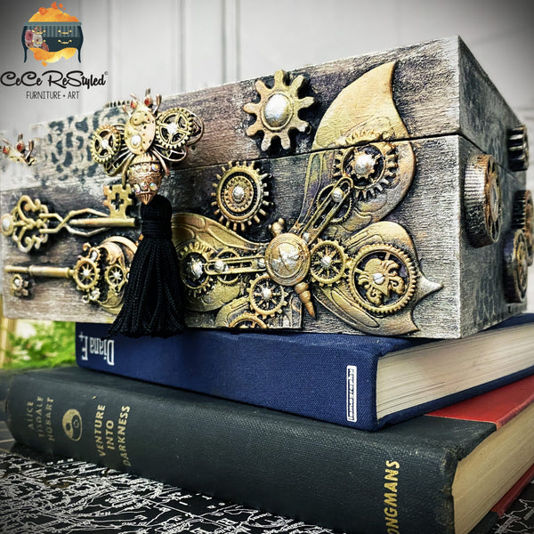 A small wood box sitting refurbished by CeCe ReStyled is painted light grey and features ReDesign with Prima's Mechanical Lock & Keys silicone mould castings in bronze color surrounded by antiquing glaze.