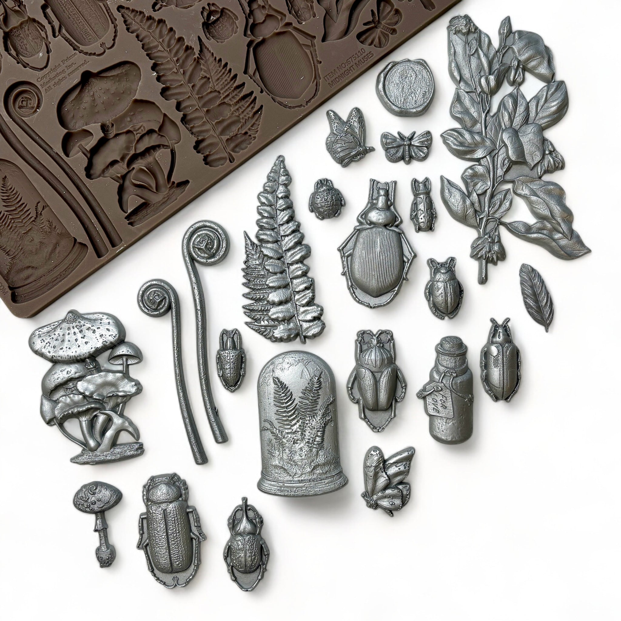 A brown silicone mold and silver colored castings of ferns, insects, mushrooms, and vintage glass containers are against a white background.