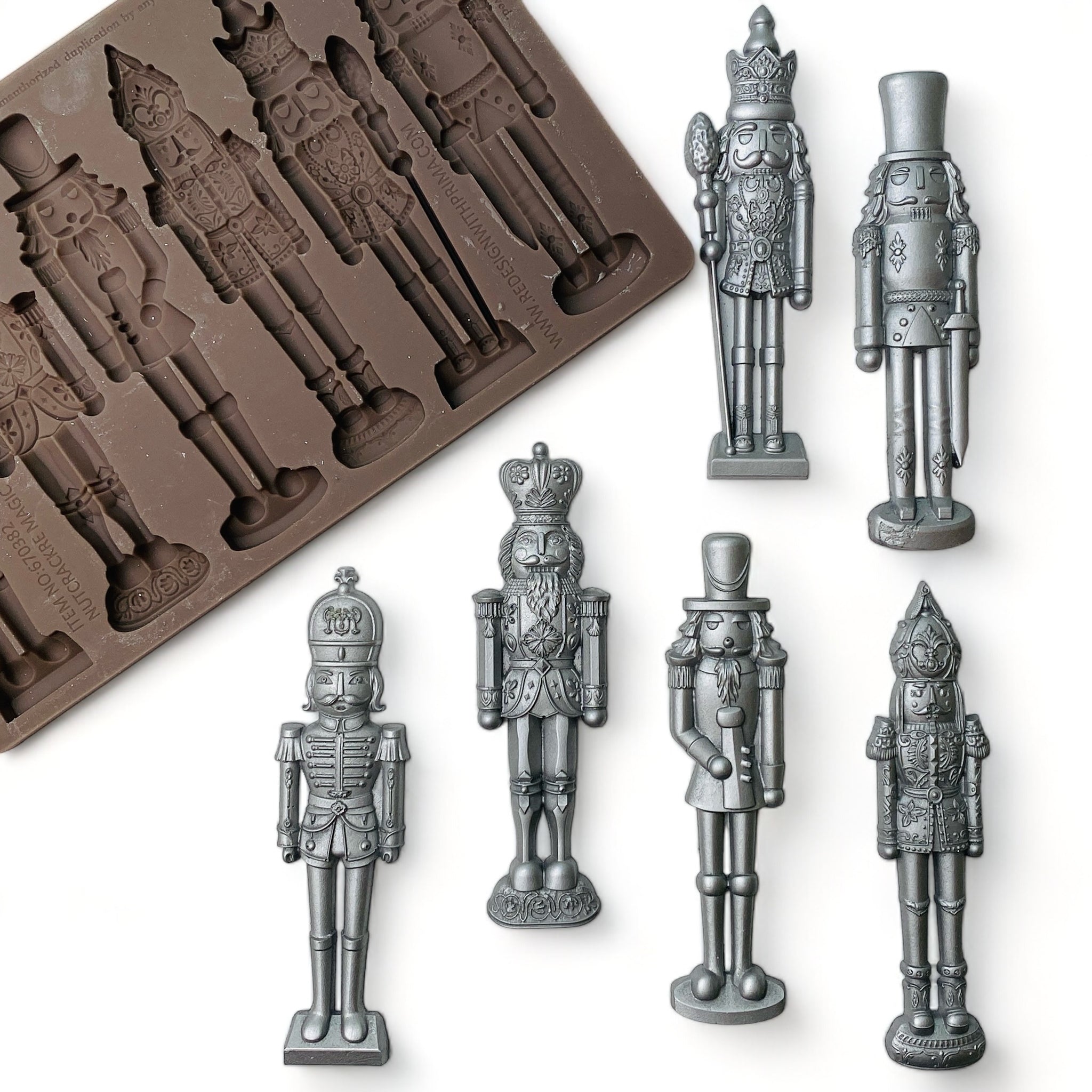 A brown silicone mold and silver colored castings of 6 ornately decorated nutcrackers are against a white background.