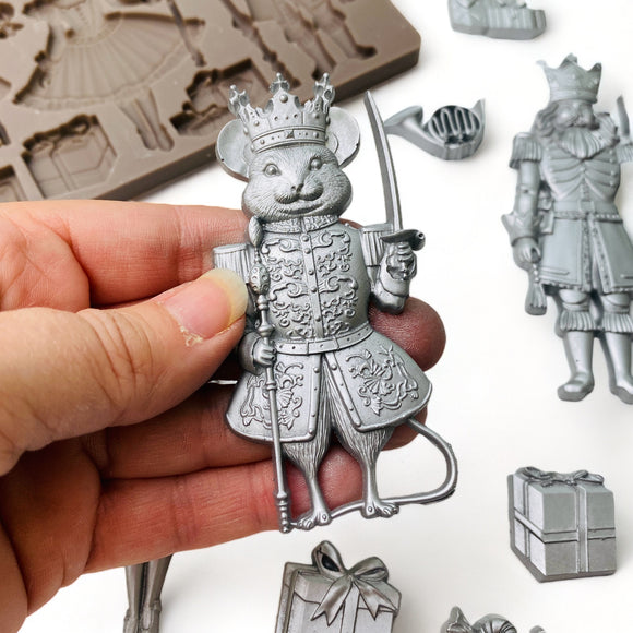 A hand is shown holding a silver colored casting of a mouse king from ReDesign with Prima's Nutcracker Party silicone mold.