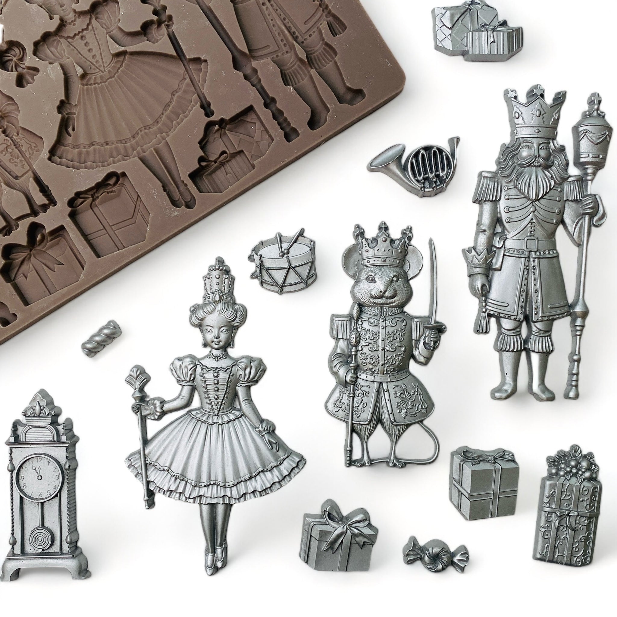 A brown silicone mold and silver colored castings of pieces and characters from The Nutcracker are against a white background.