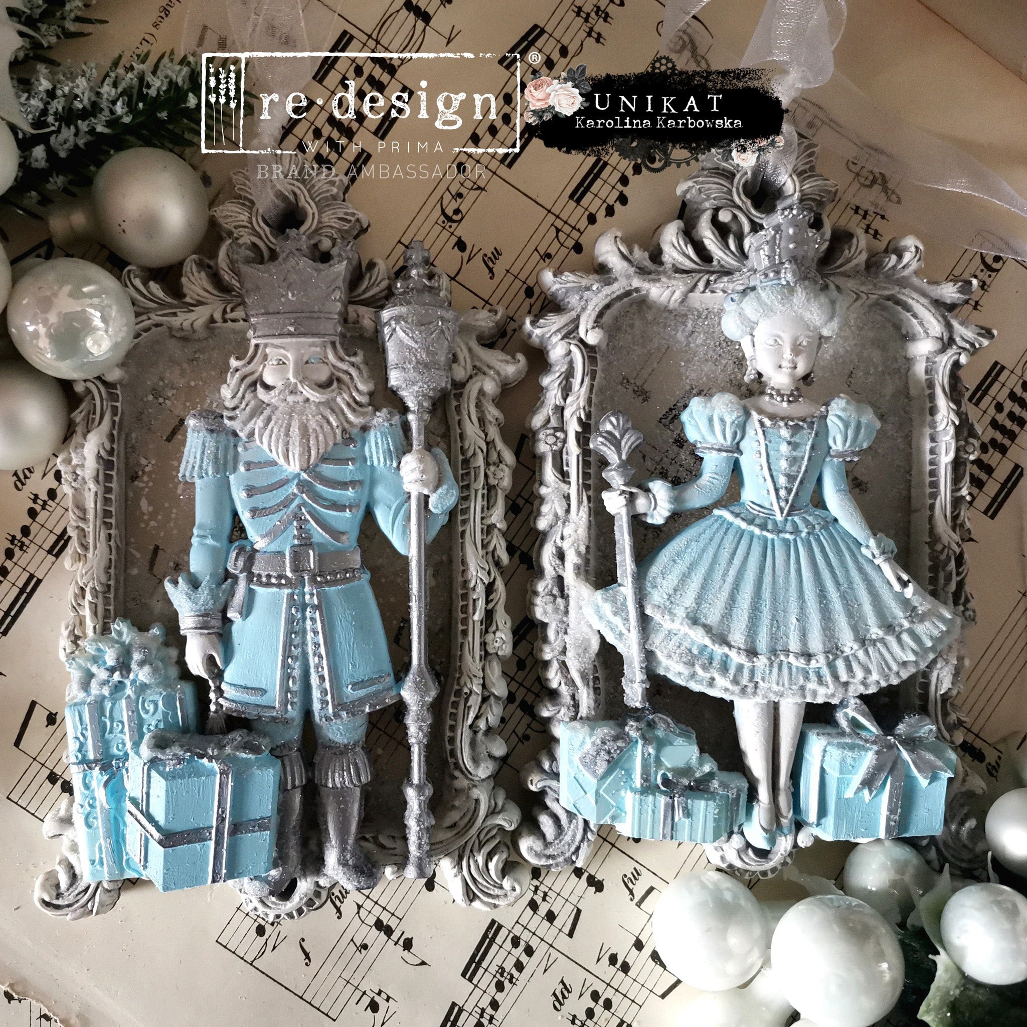 Blue pastel painted castings of a king and queen and Christmas gifts created by Unikat Karolina Karboska using ReDesign with Prima's Nutcracker Party silicone mold are shown against a sheet of music.