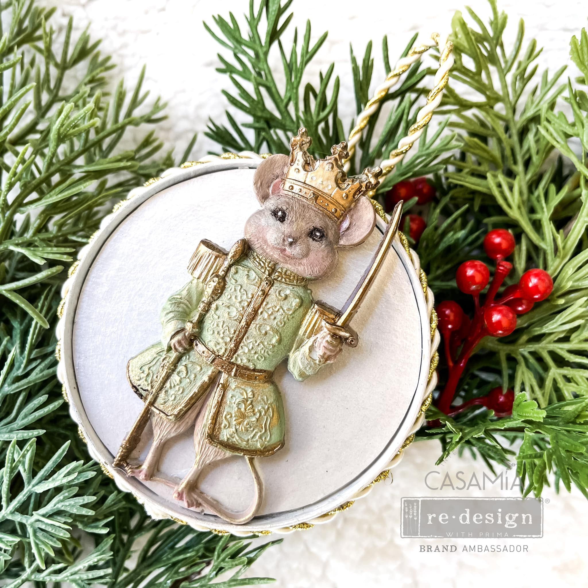 A round flat ornament against a pine tree sprig created by Casamia features the mouse king from ReDesign with Prima's Nutcracker Party silicone mold on it.