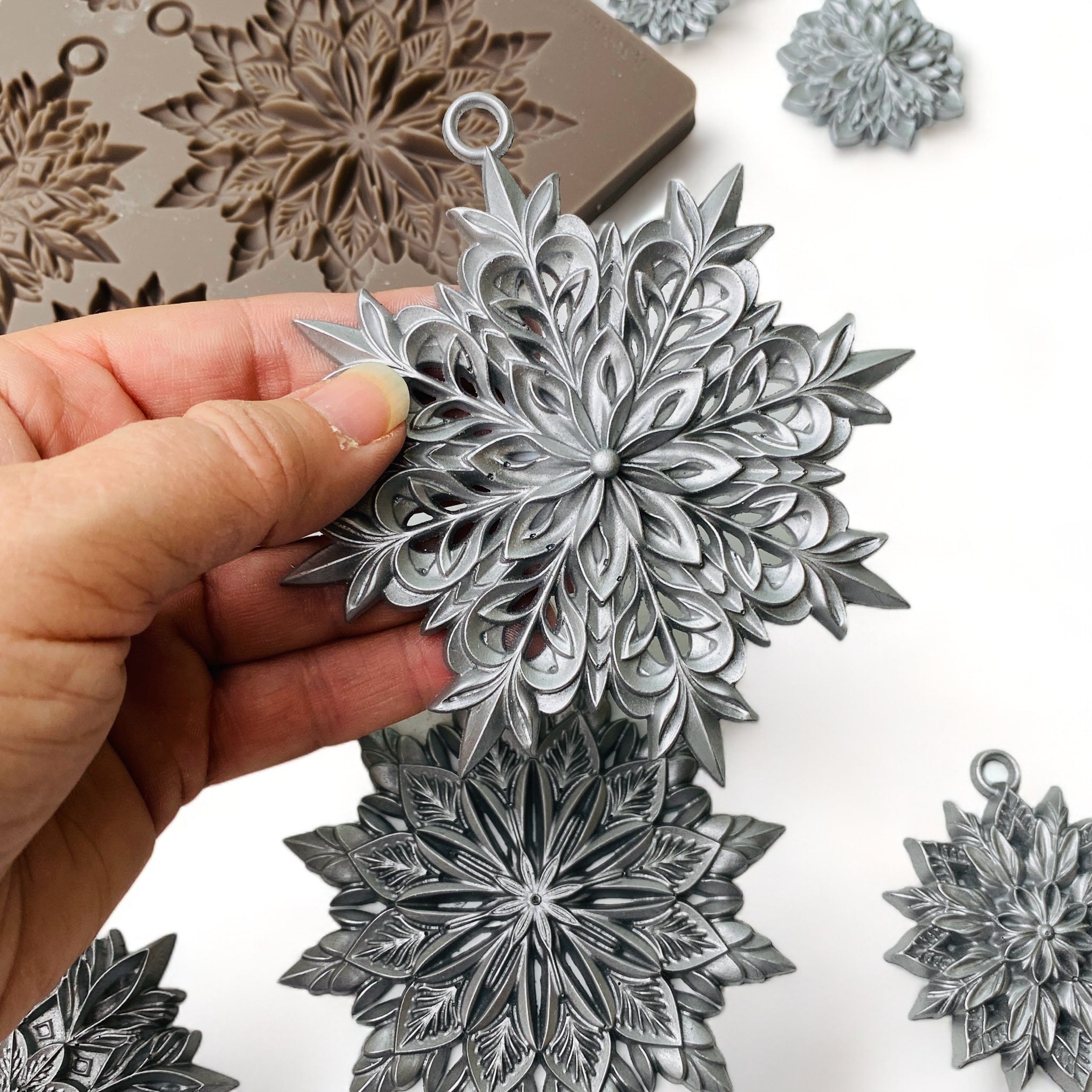 A hand is shown holding a large snowflake from ReDesign with Prima's Papercraft Charms silicone mold.