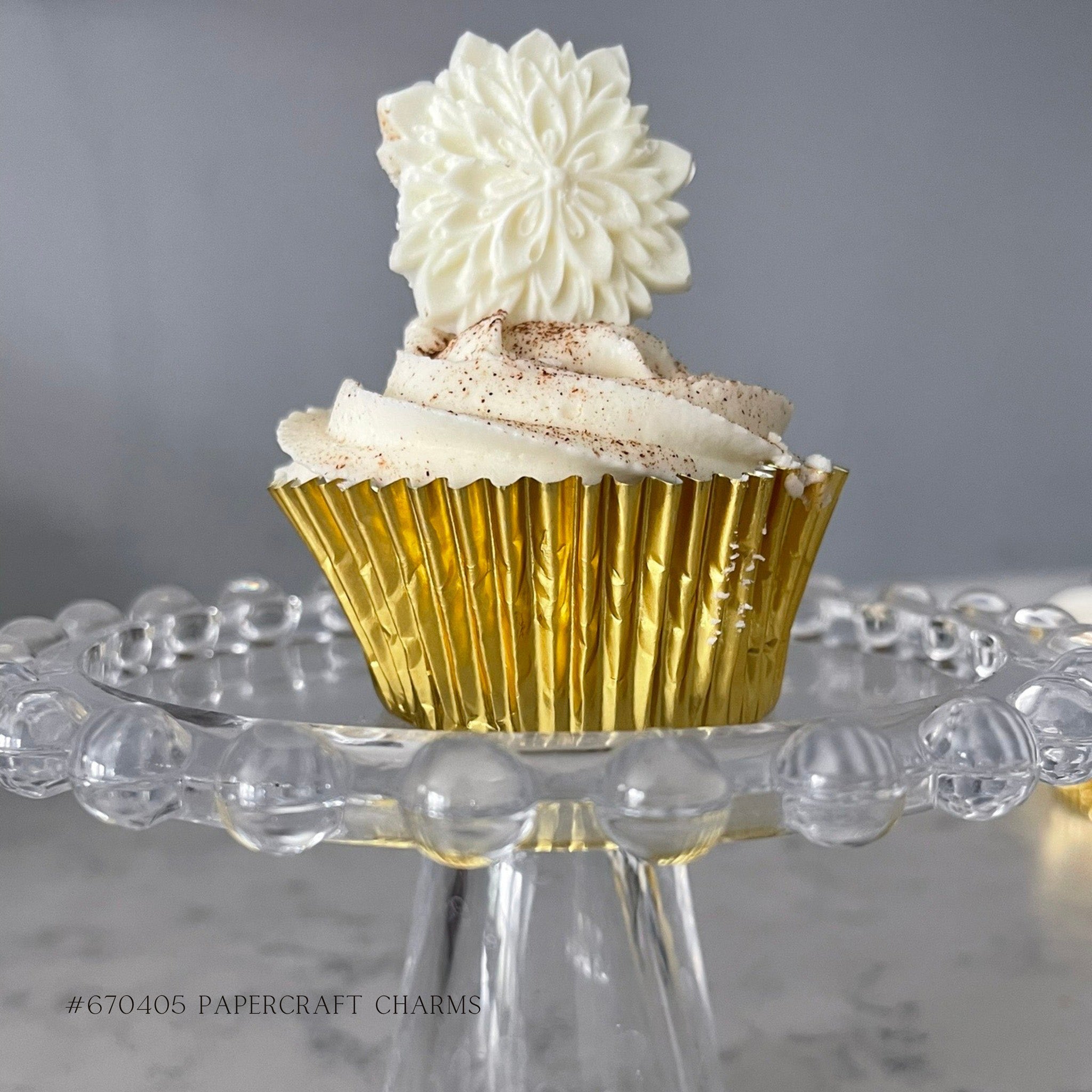 A cupcake with white frosting is in a gold cupcake paper cup and features a casting made out of white chocolate from ReDesign with Prima's Papercraft Charms silicone mold.