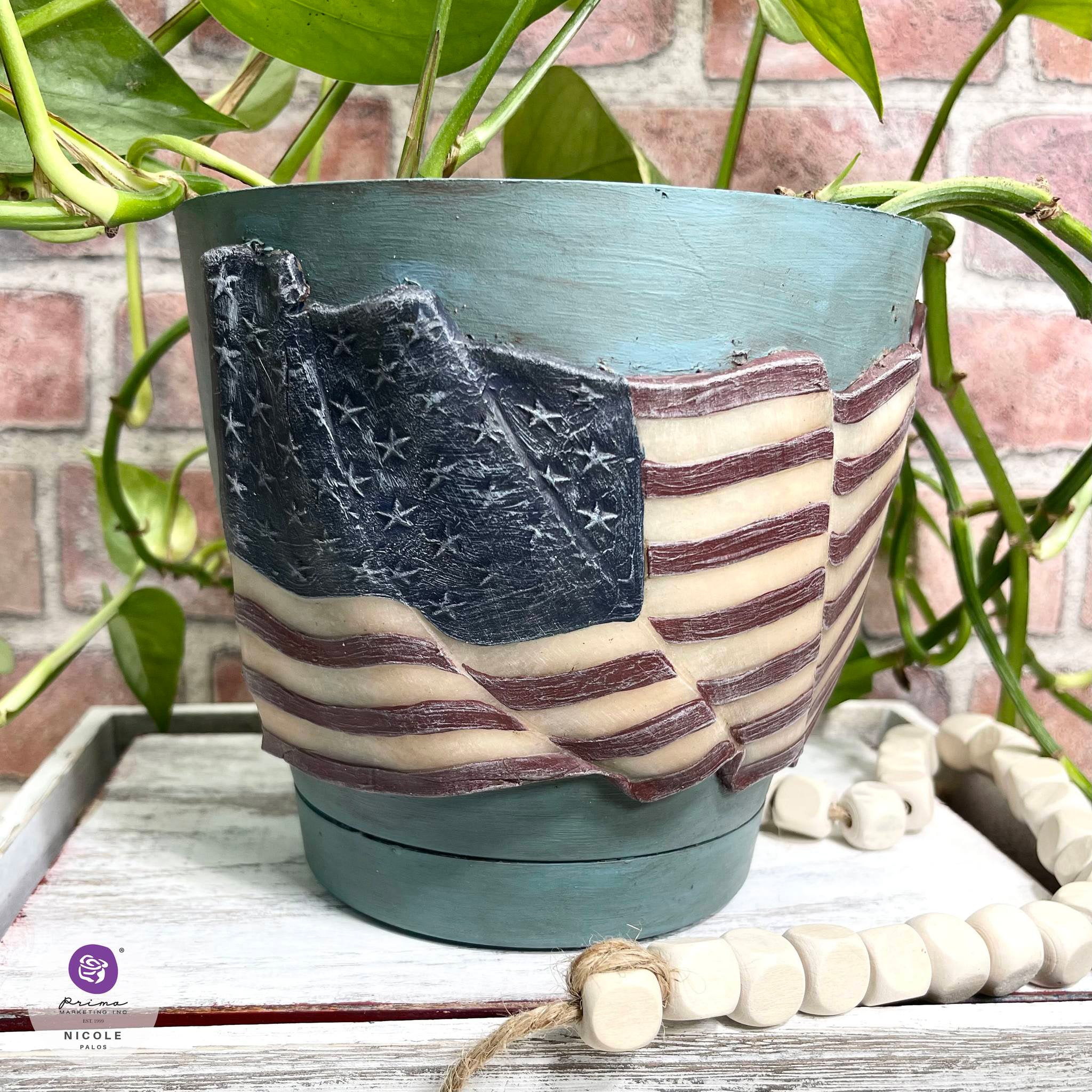 A small planter pot is painted light teal blue and features a colorfully painted casting of ReDesign with Prima's Star Spangled silicone mold on it.