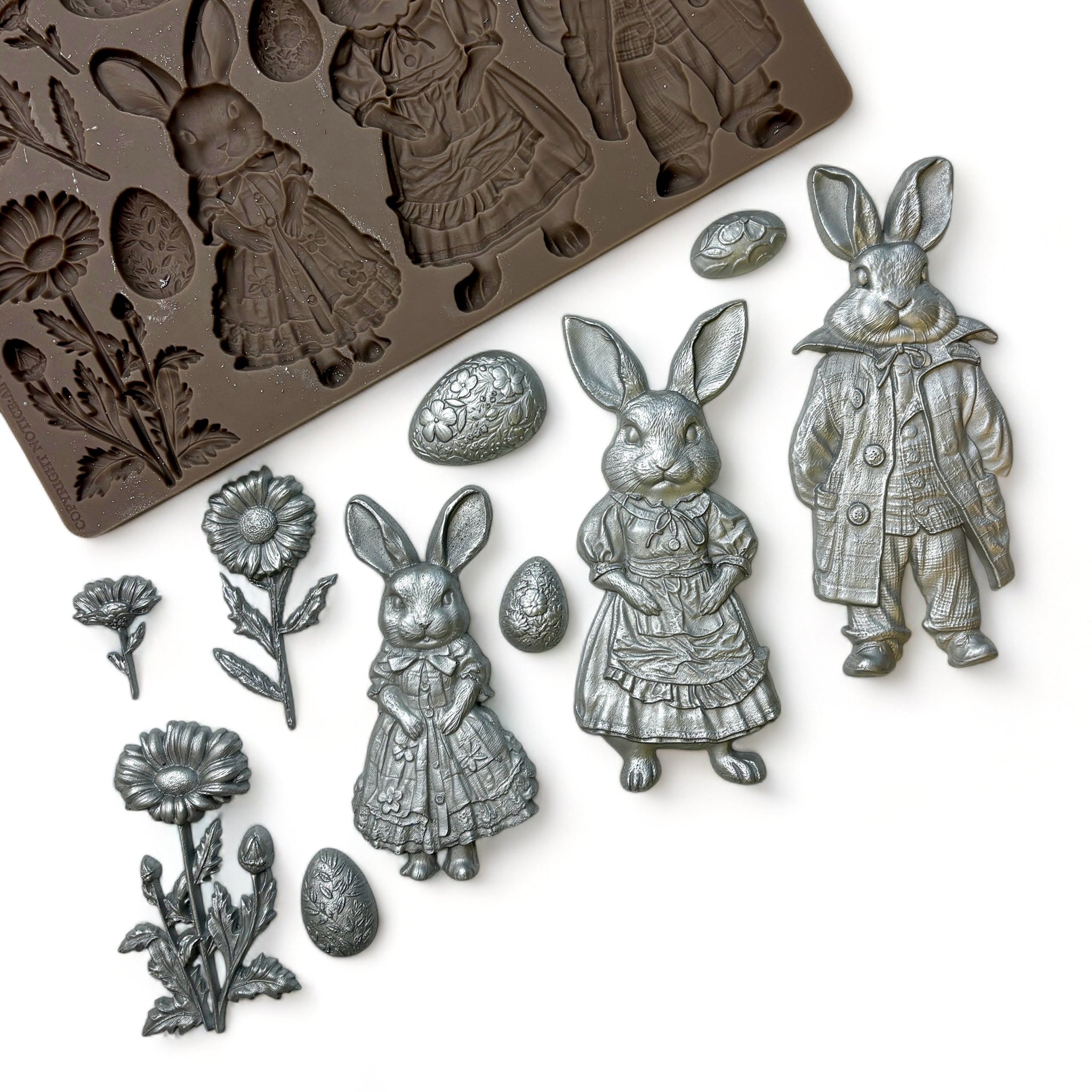 A brown silicone mold and silver colored castings of 3 cute bunnies in clothes, 3 flowers, and 4 Easter eggs are against a white background.