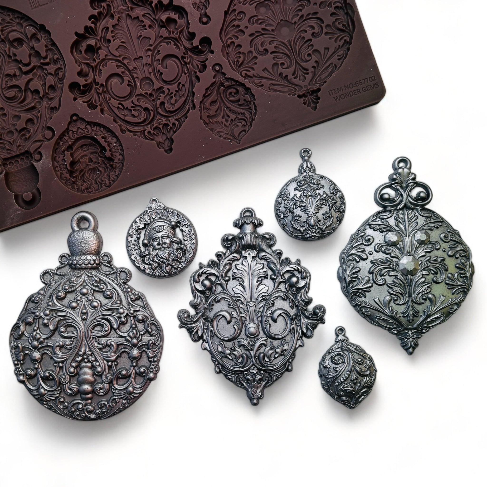 A brown silicone mold and silver colored castings of 6 varying size ornately decorated tree ornaments are against a white background.