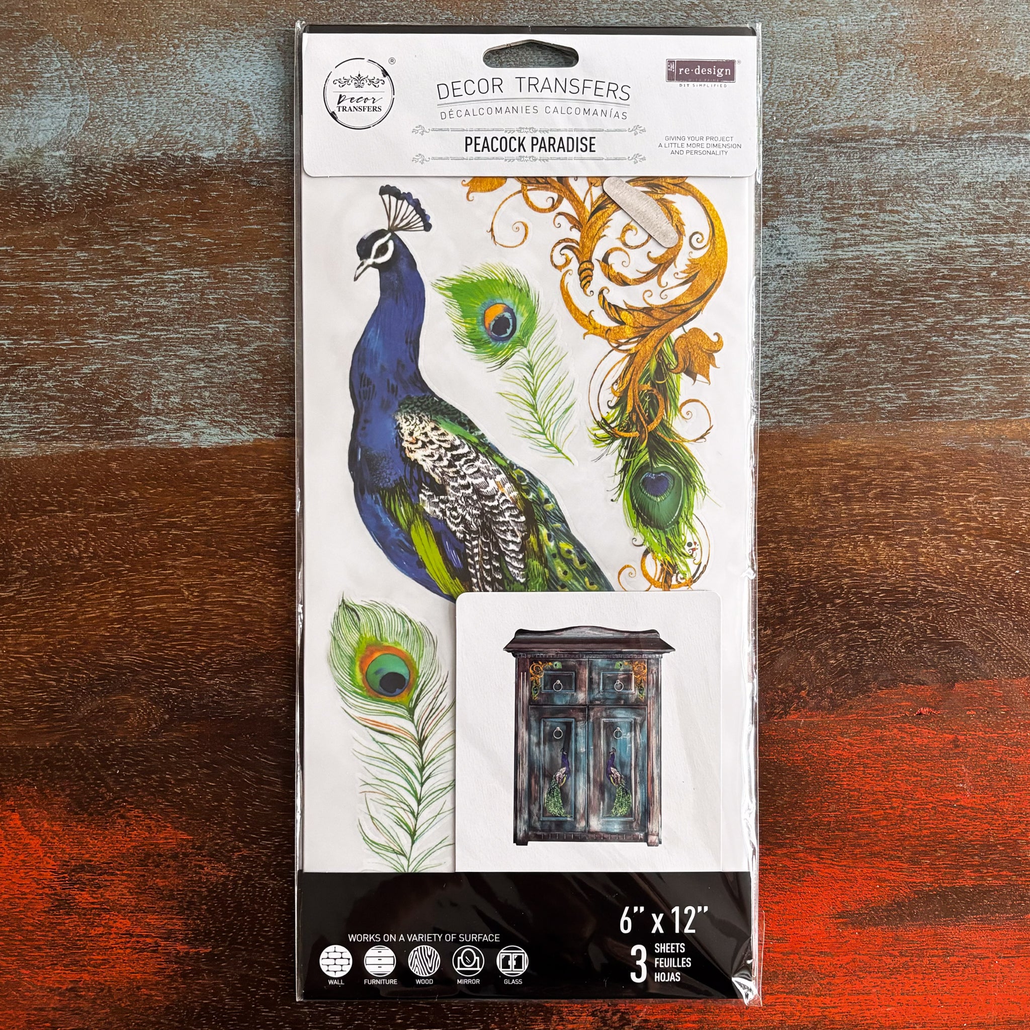 A package of ReDesign with Prima's Peacock Paradise small transfer is against a dark wood background.