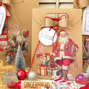 A brown paper gift bag has a white round gift tag that features ReDesign with Prima's Merry and Bright decor stamp on it.