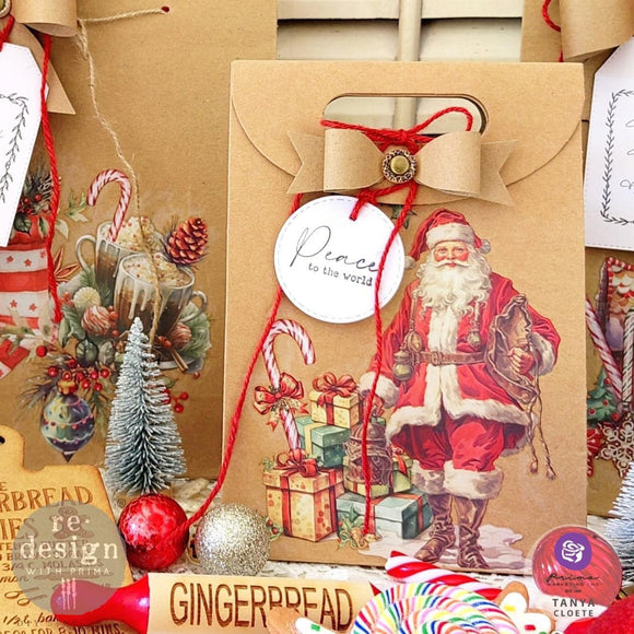 A brown paper gift bag has a white round gift tag that features ReDesign with Prima's Merry and Bright decor stamp on it.
