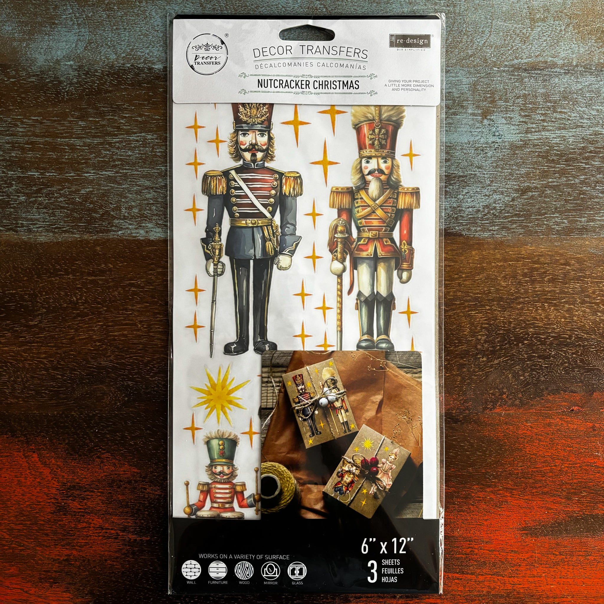 A package of ReDesign with Prima's Nutcracker Christmas small rub-on transfer is against a dark wood background.