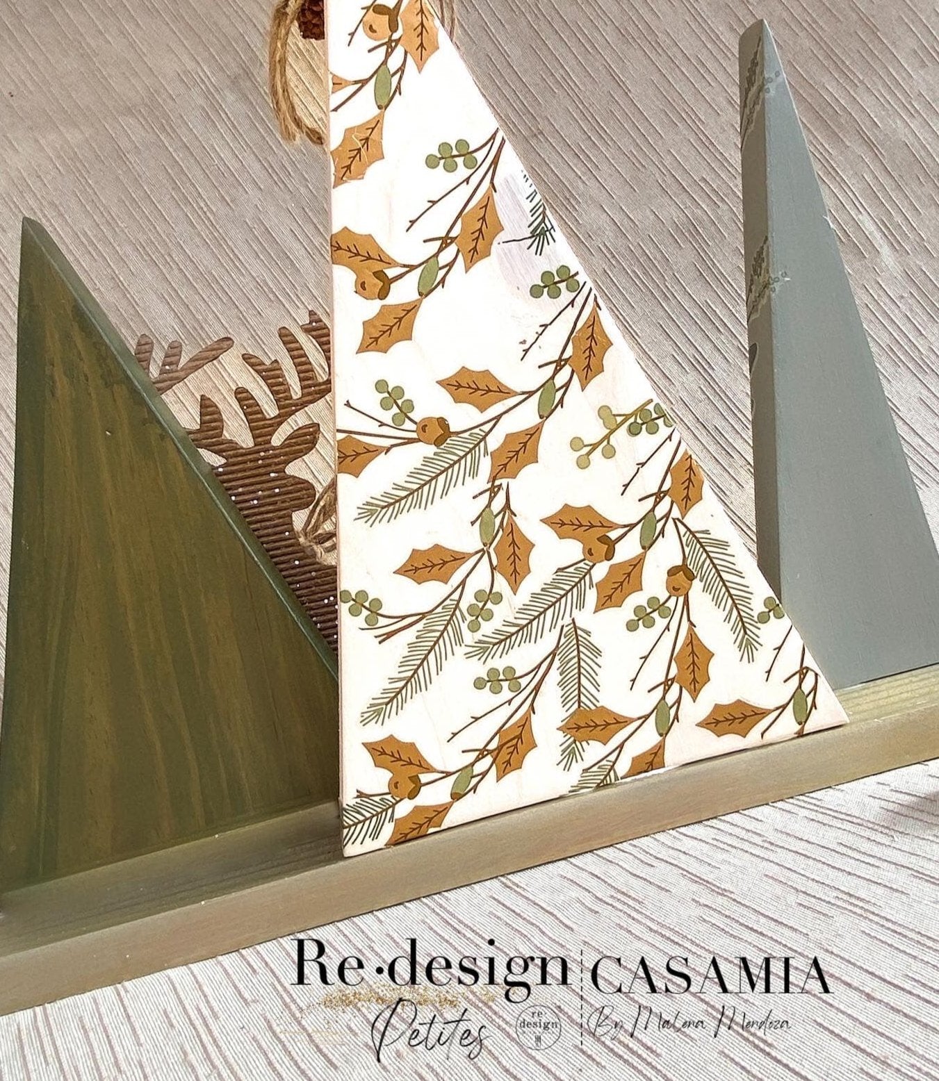 A wood craft features 3 triangular pine trees created by Casamia. The largest center tree is painted white and features a part of ReDesign with Prima's Holiday Spirit small transfer on it.