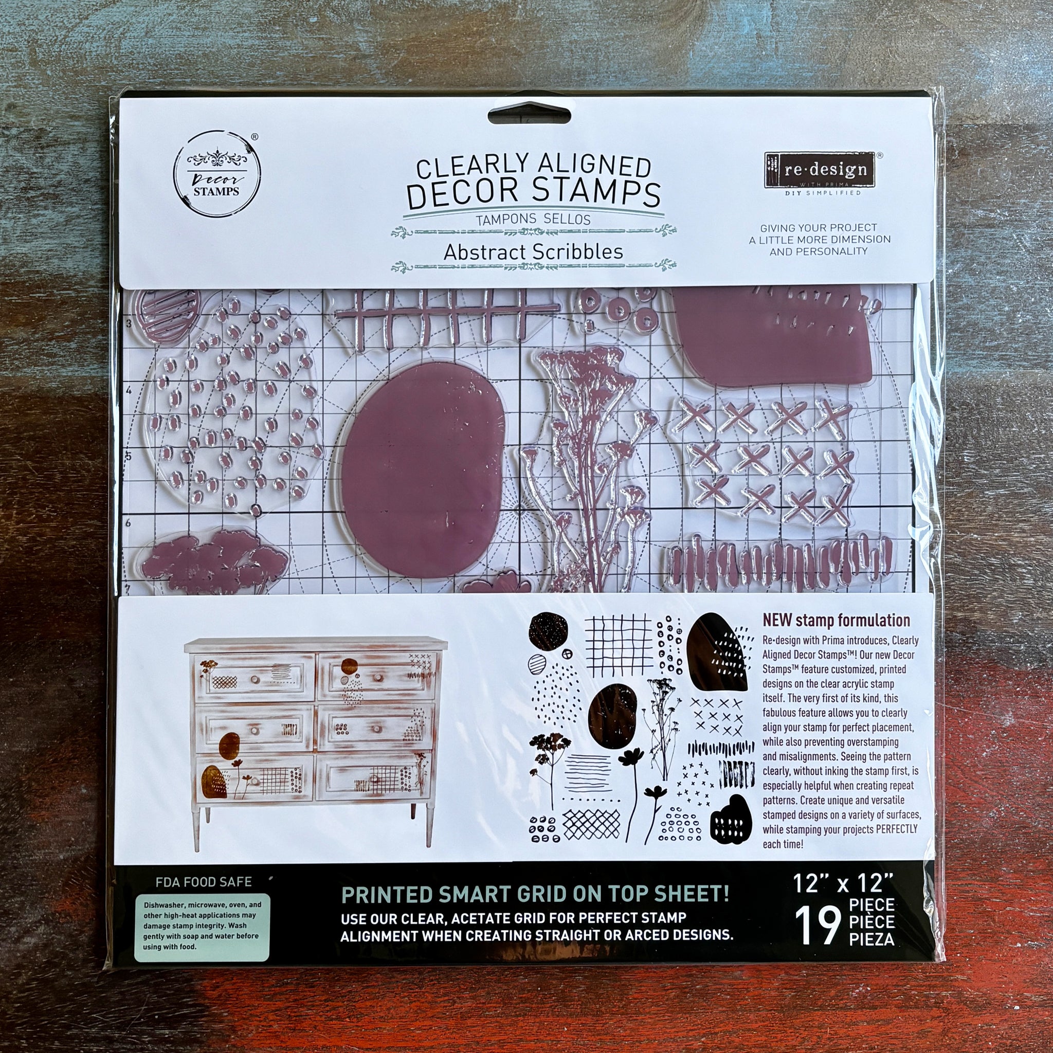 A package of ReDesign with Prima's Abstract Scribbles Clearly Aligned decor stamps is against a dark wood background.