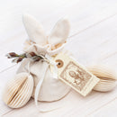 A bunny shaped cream colored gift sack features a handmade gift tag that features 1 of ReDesign with Prima's Easter Blessings stamp on it are against a white wood table.