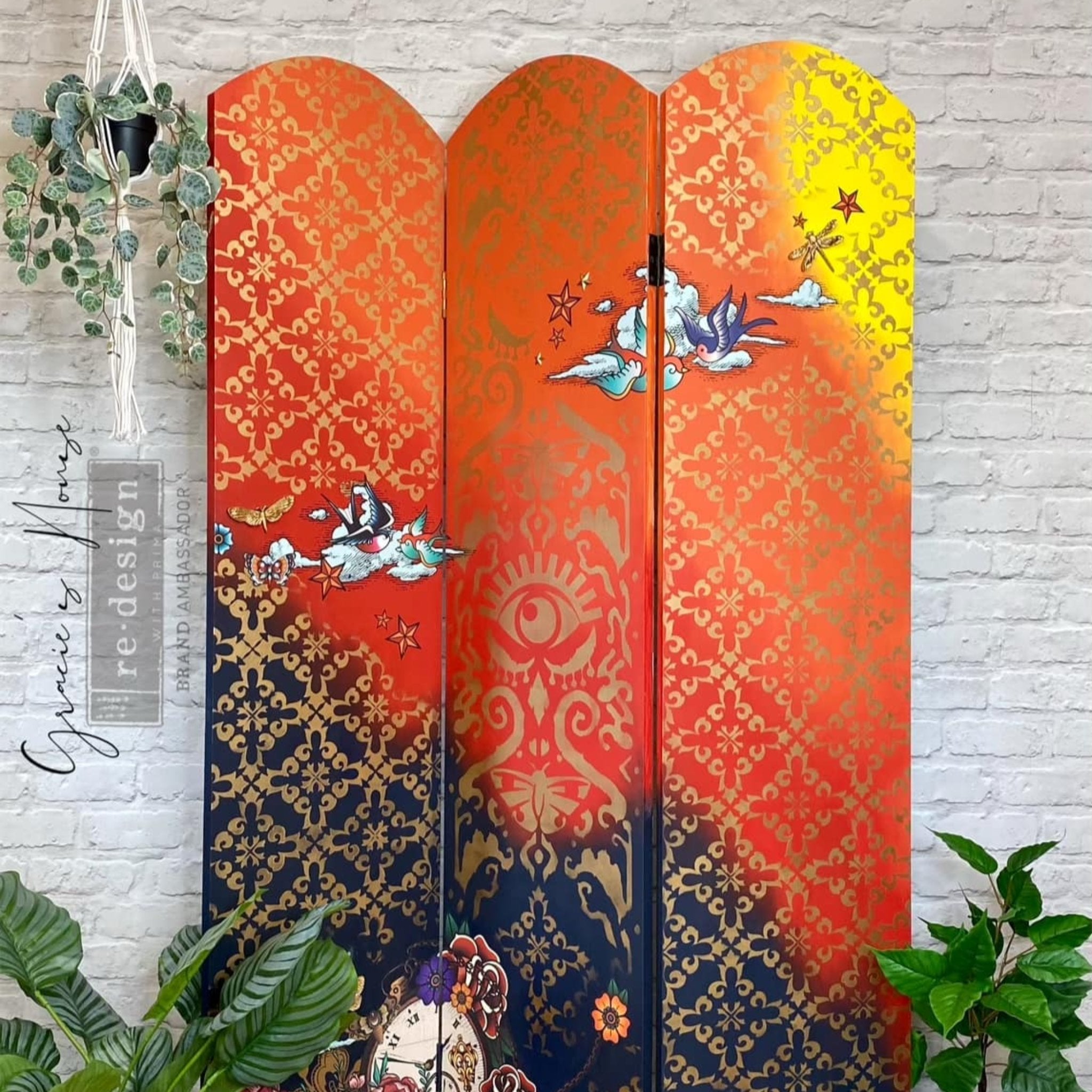 A 3-fold room divider refurbished by Gracie's House is painted a blend of yellow, orange, and dark blue and features ReDesign with Prima's All Seeing Ikat stencil in gold on it.