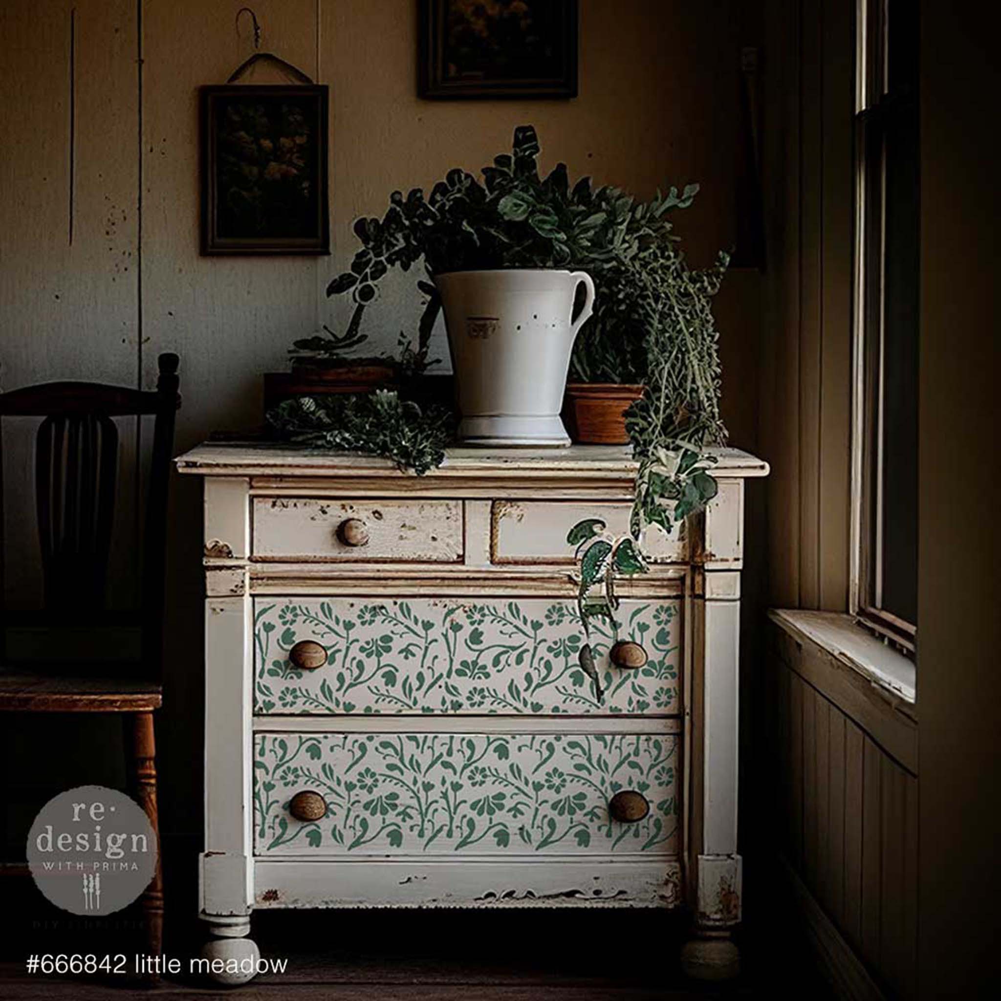 A vintage 4-drawer dresser painted light beige features ReDesign with Prima's Little Meadow stencil in green on the bottom 2 drawers.