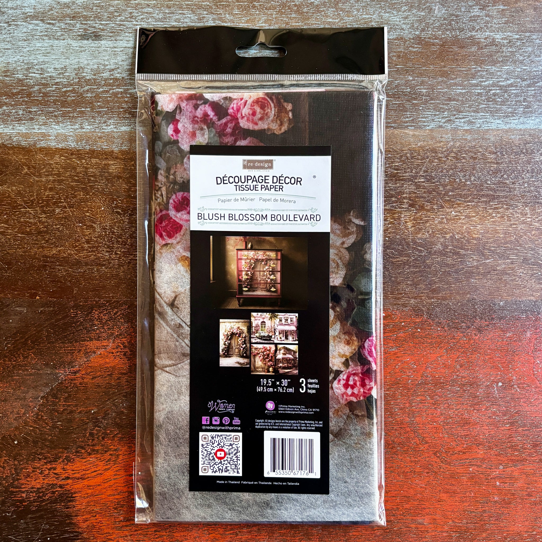 A package of ReDesign with Prima's Blush Blossom Boulevard tissue paper is against a dark wood background.