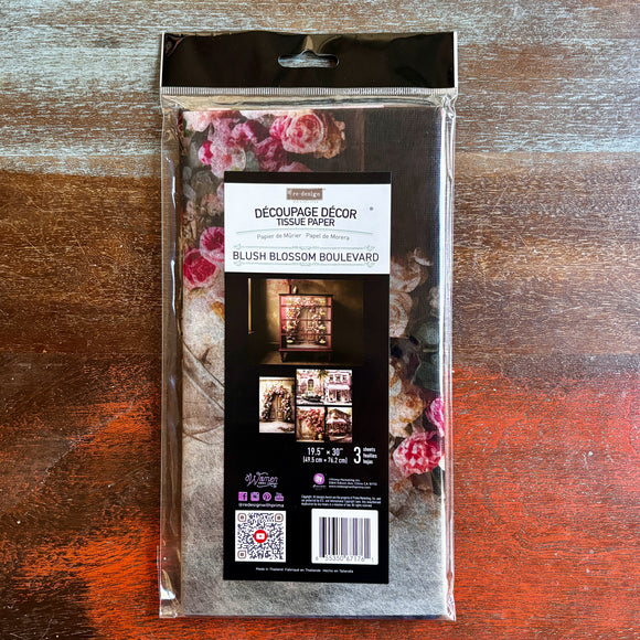 A package of ReDesign with Prima's Blush Blossom Boulevard tissue paper is against a dark wood background.