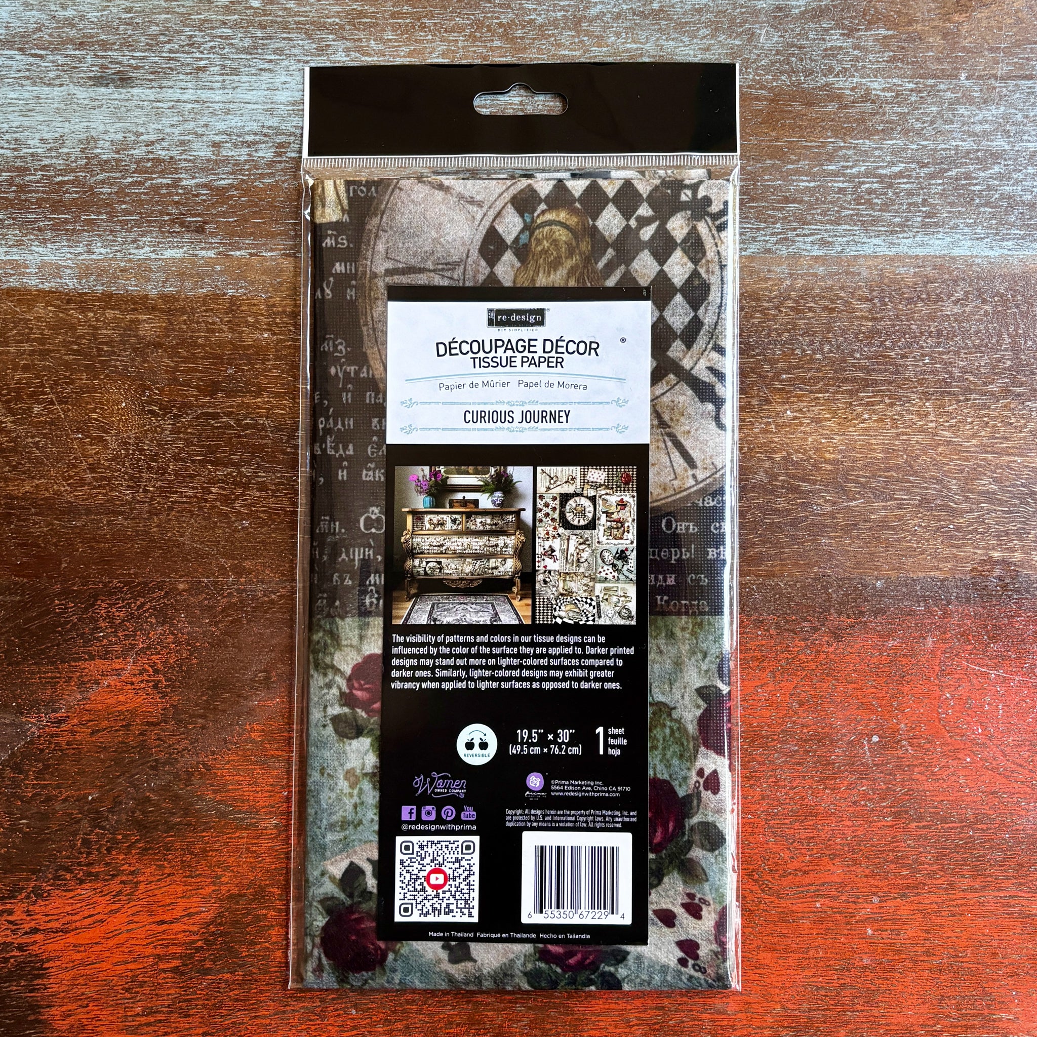 A package of ReDesign with Prima's Curious Journey tissue paper is against a dark wood background.